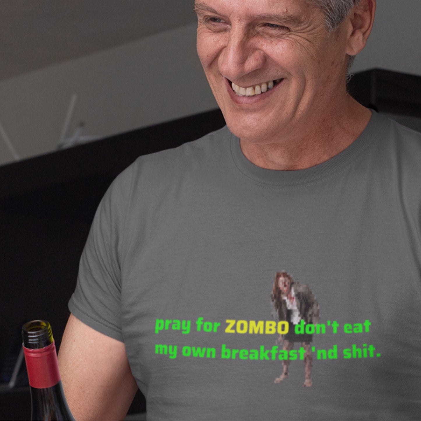 Man wearing a gray t-shirt with a graphic and text, sitting next to a bottle.