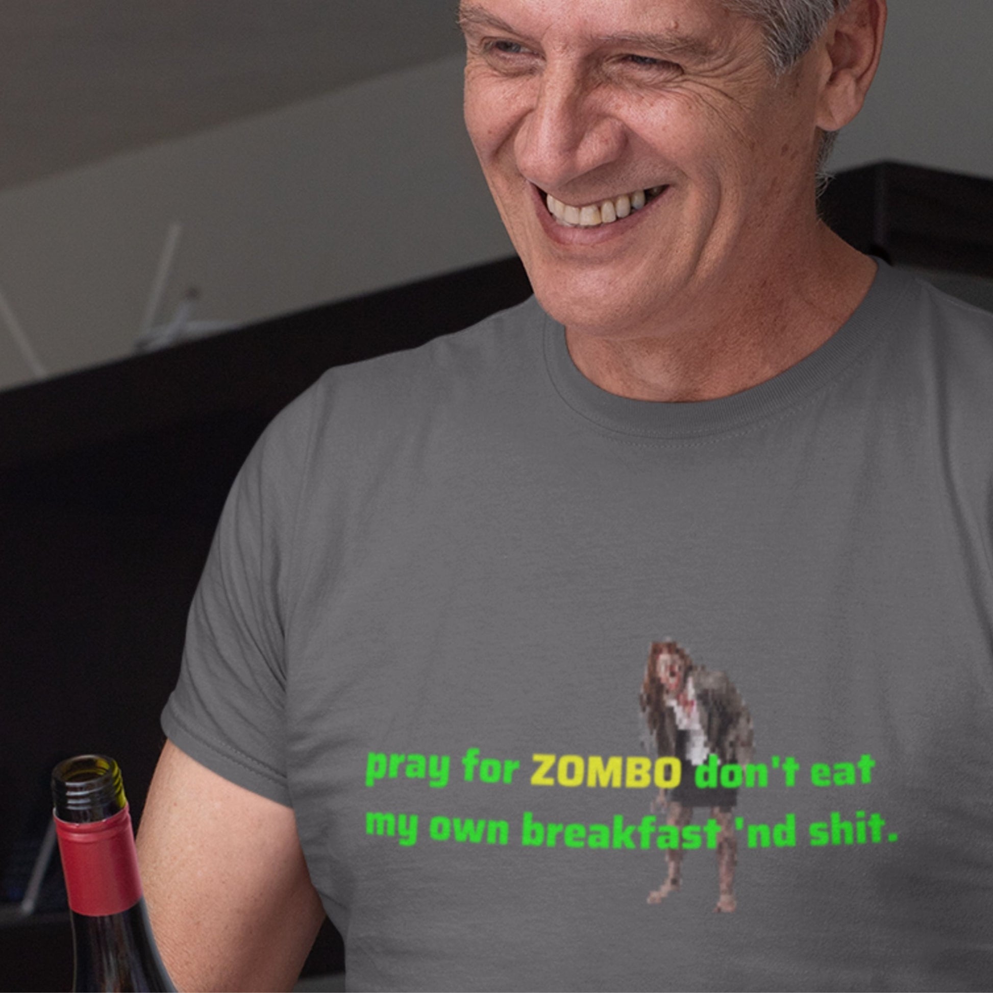 Man wearing a gray t-shirt with a graphic and text, sitting next to a bottle.