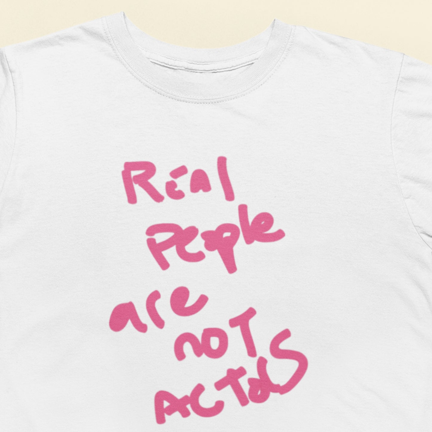 White t-shirt with pink text 'Real people are not actors' on a light beige background