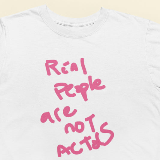 White t-shirt with pink text 'Real people are not actors' on a light beige background