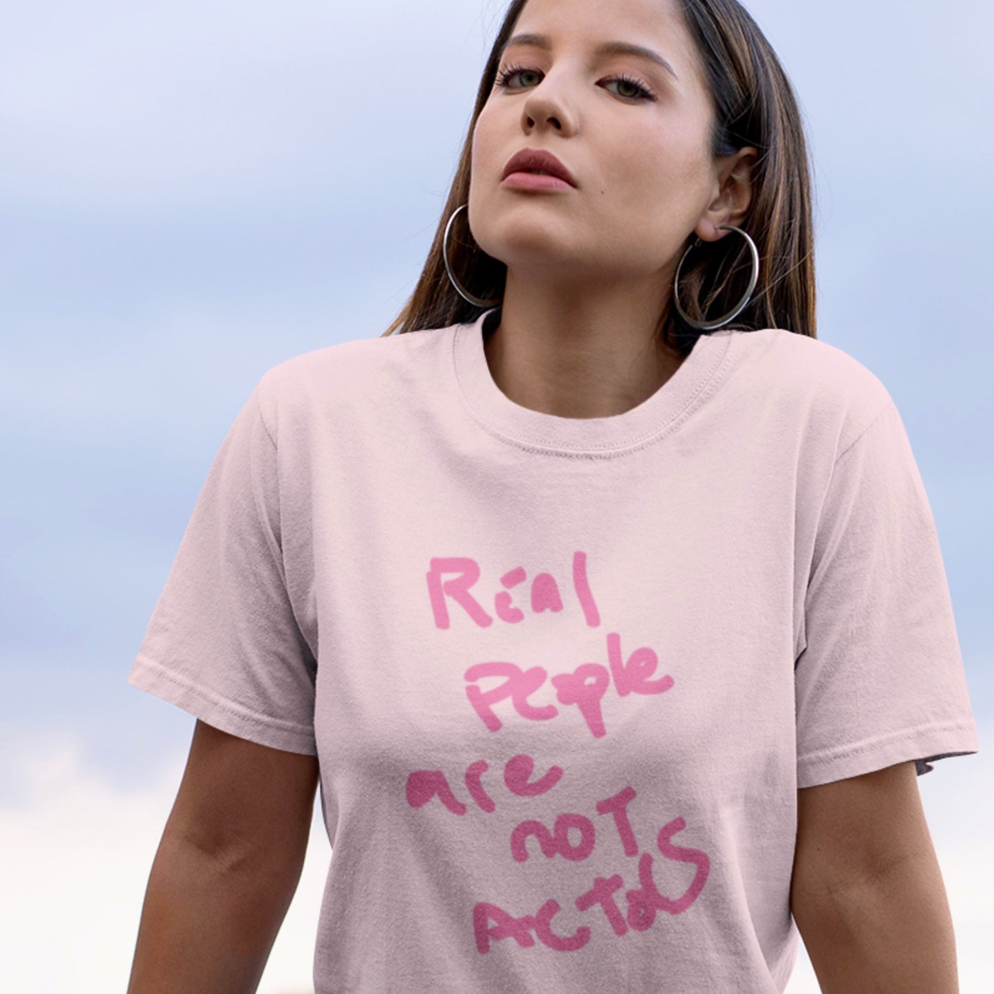 Woman wearing a light pink t-shirt with pink text against a blue sky.