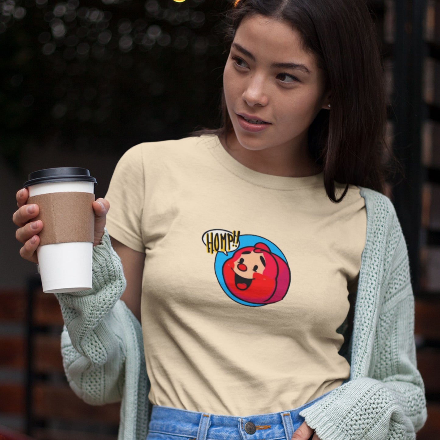 Woman wearing a beige t-shirt with a colorful graphic design, holding a coffee cup.
