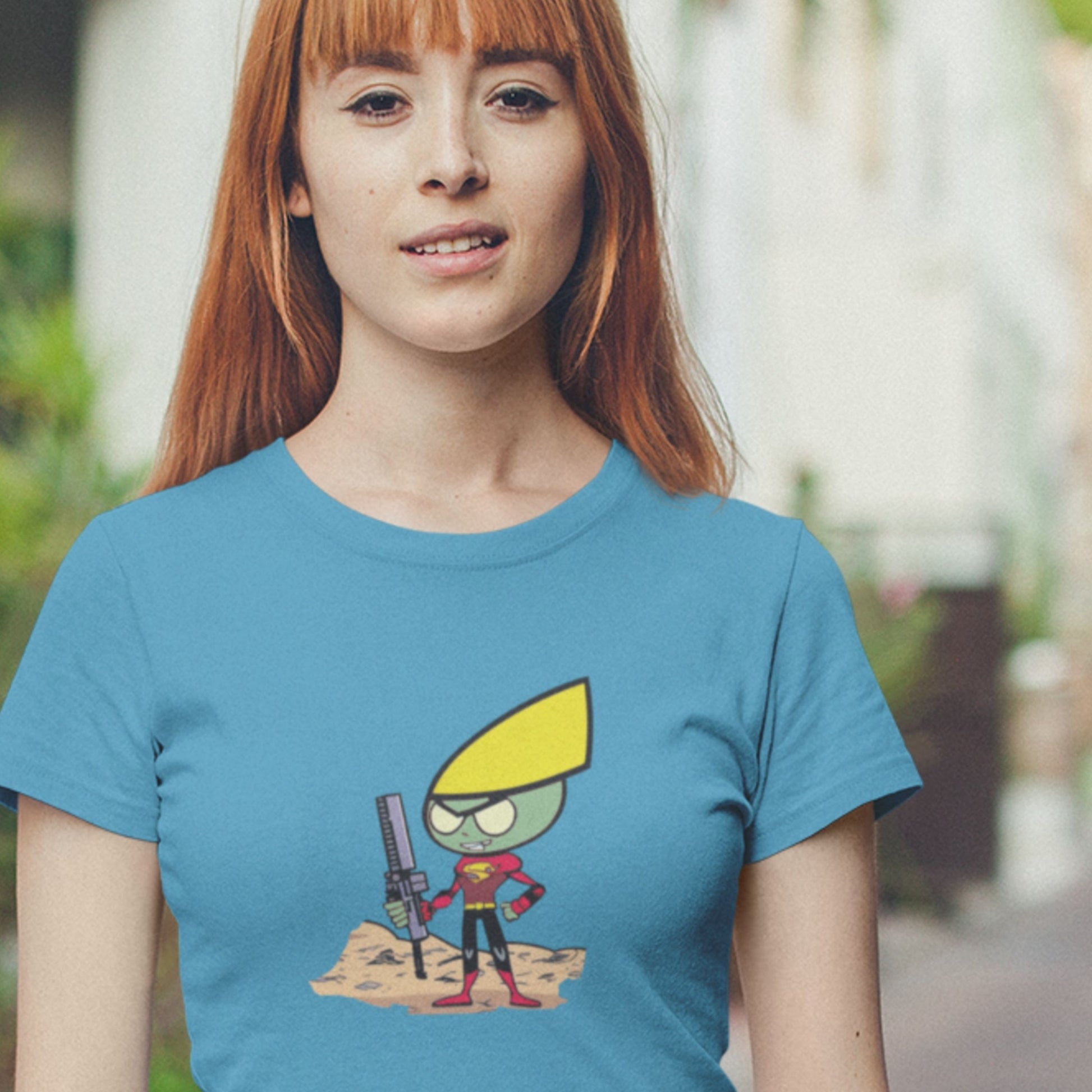Smiling woman wearing an aqua blue shirt with a fun, colorful cartoon illustration outdoors.