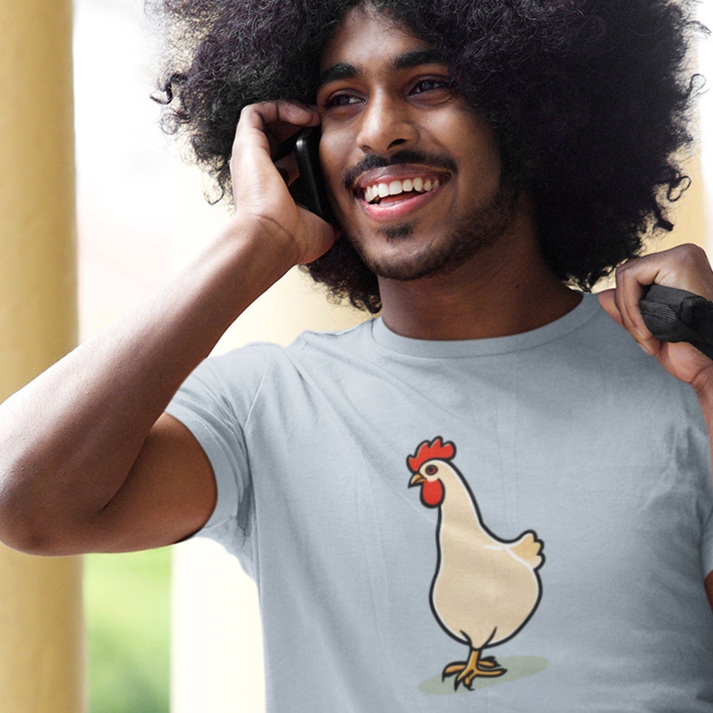 Man wearing a t-shirt with a cartoon chicken design, talking on a phone.