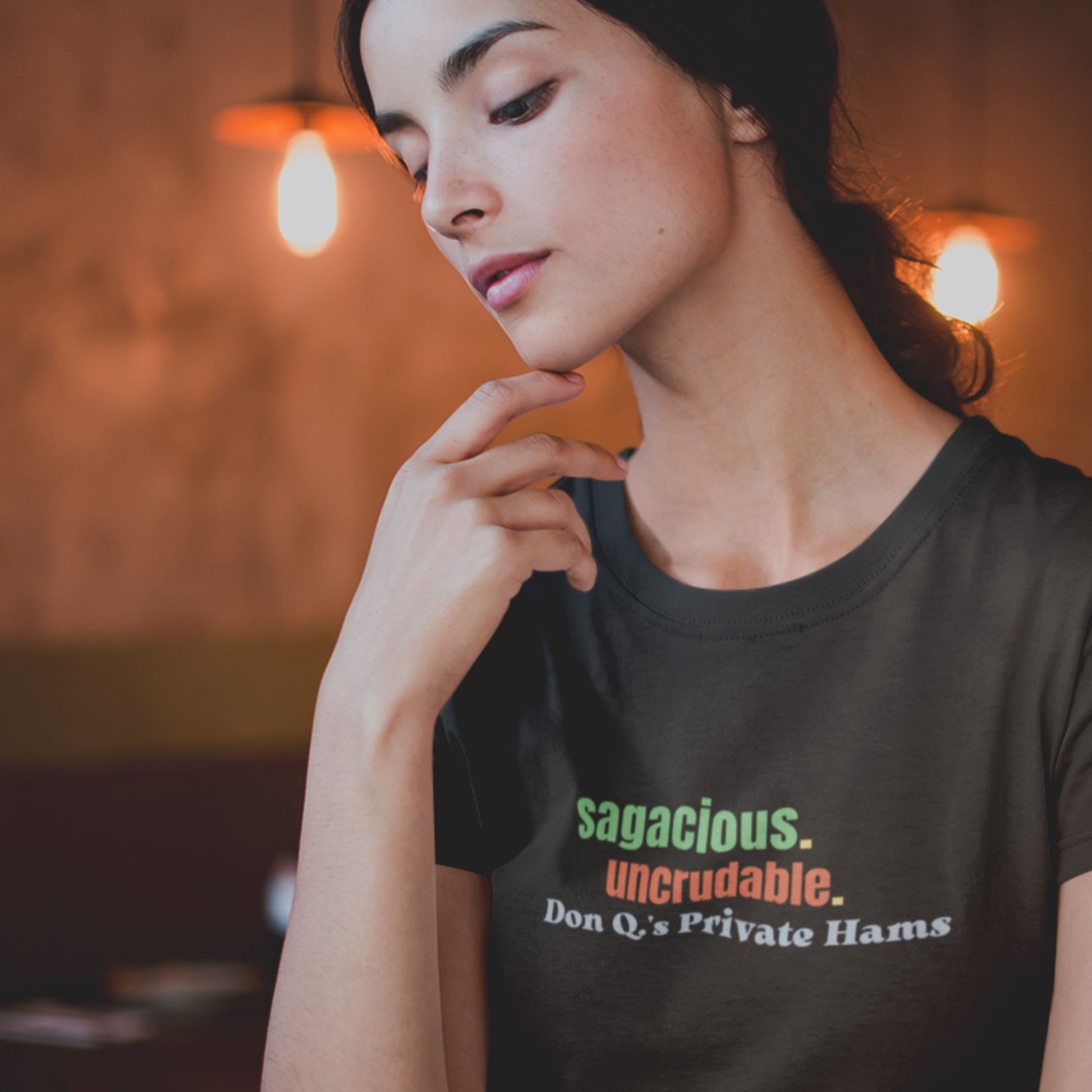 Pensive woman wearing a black t-shirt with humorous colorful text in a dark restaurant.