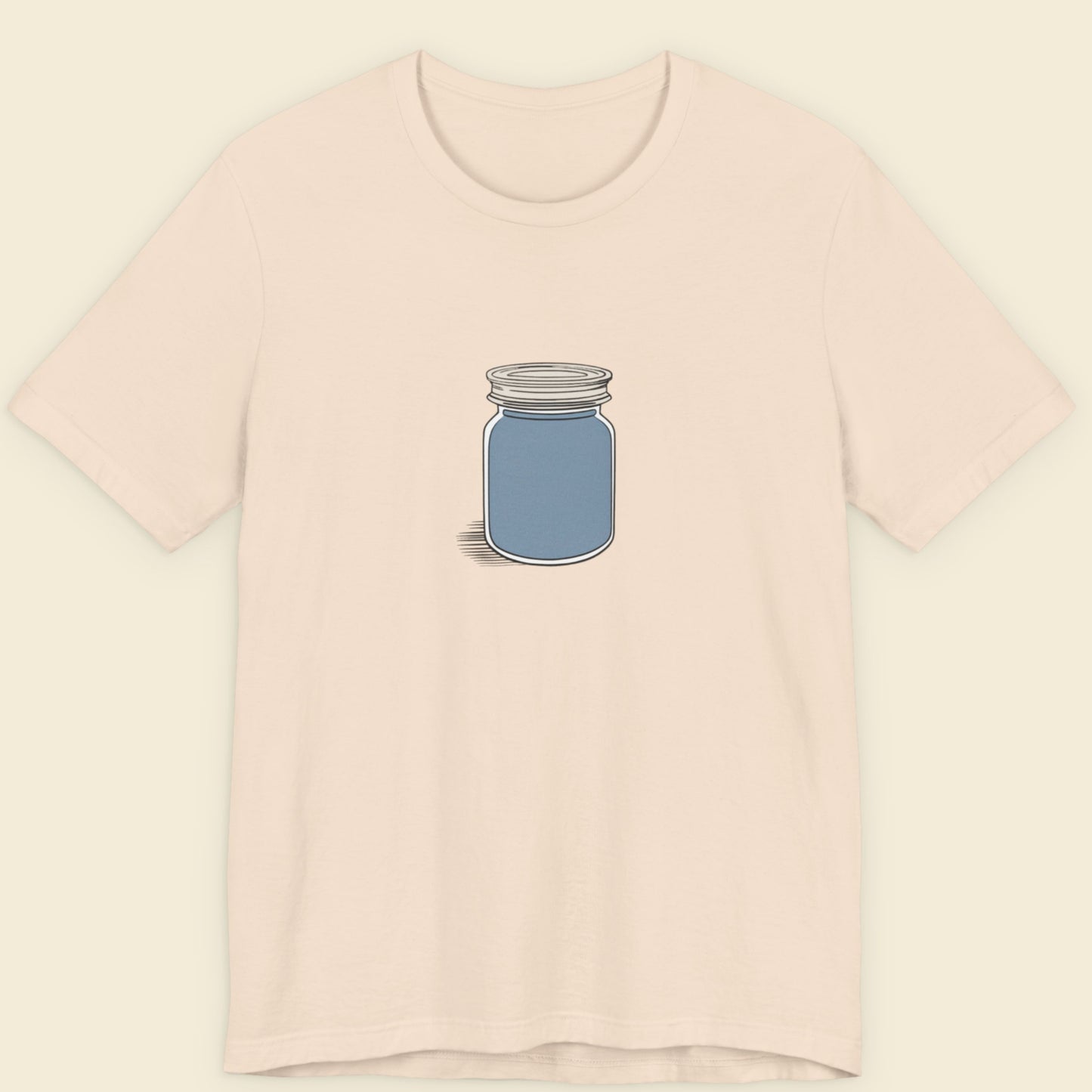 Beige shirt with a drawing of a screw top jar full of something blue.