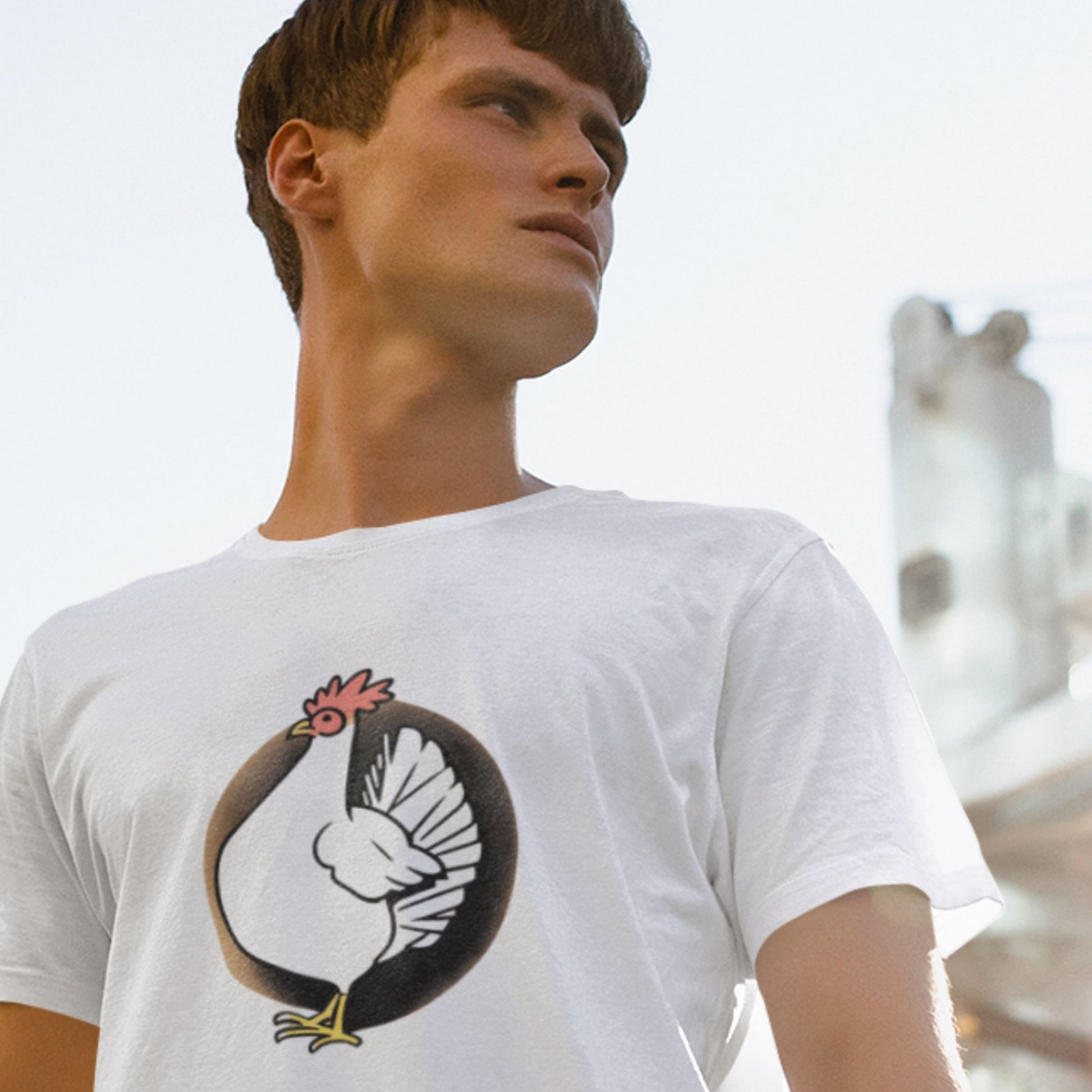Man wearing a white t-shirt with a graphic design of a chicken, standing outdoors.