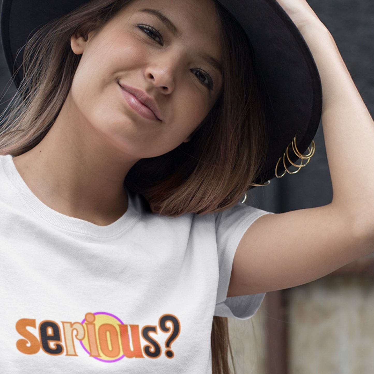 Woman wearing a white t-shirt with 'serious?' text, posing with a black hat.