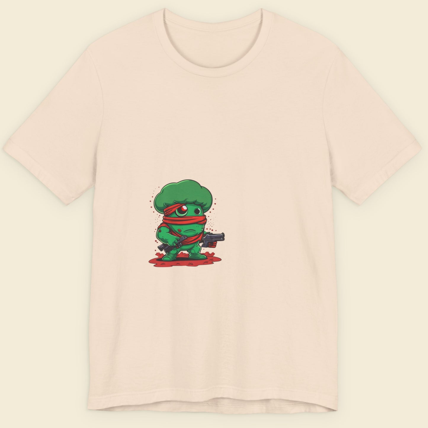 Pink t-shirt with a green cartoon character holding a gun on a beige background.