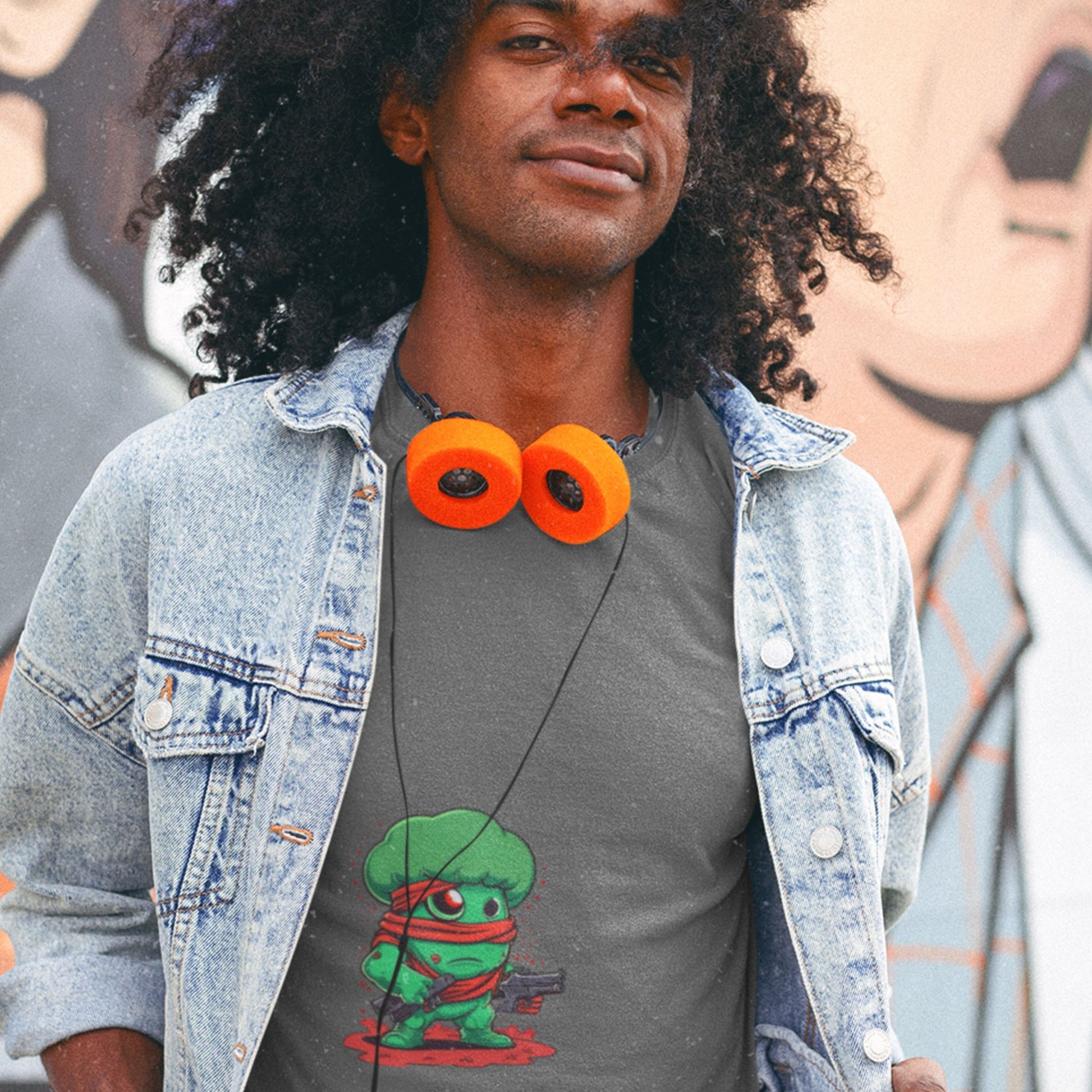 Man wearing a denim jacket and a t-shirt with a graphic design, standing in front of a graffiti wall.