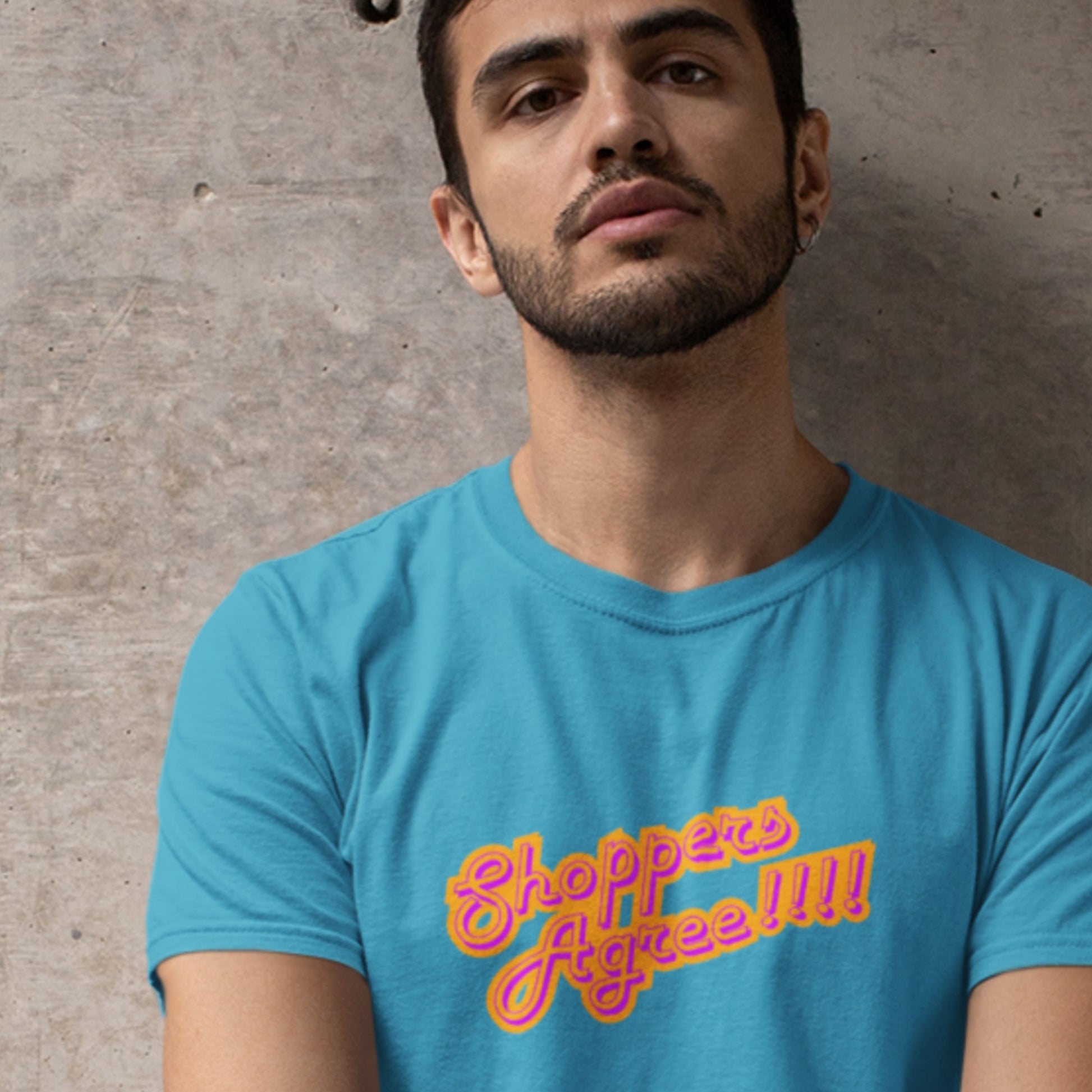 Man standing wearing a blue t-shirt with humorous colorful text on a grey background.