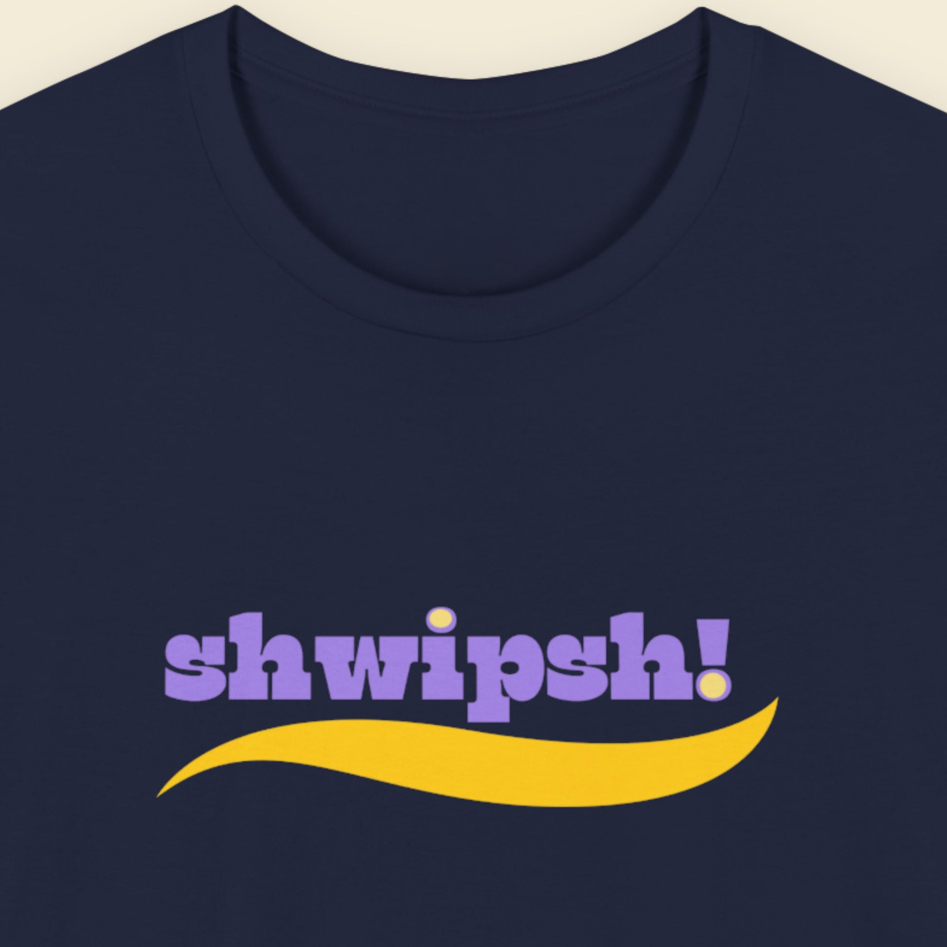 Navy blue t-shirt with multicolored 'shwipsh!' text on a beige background.