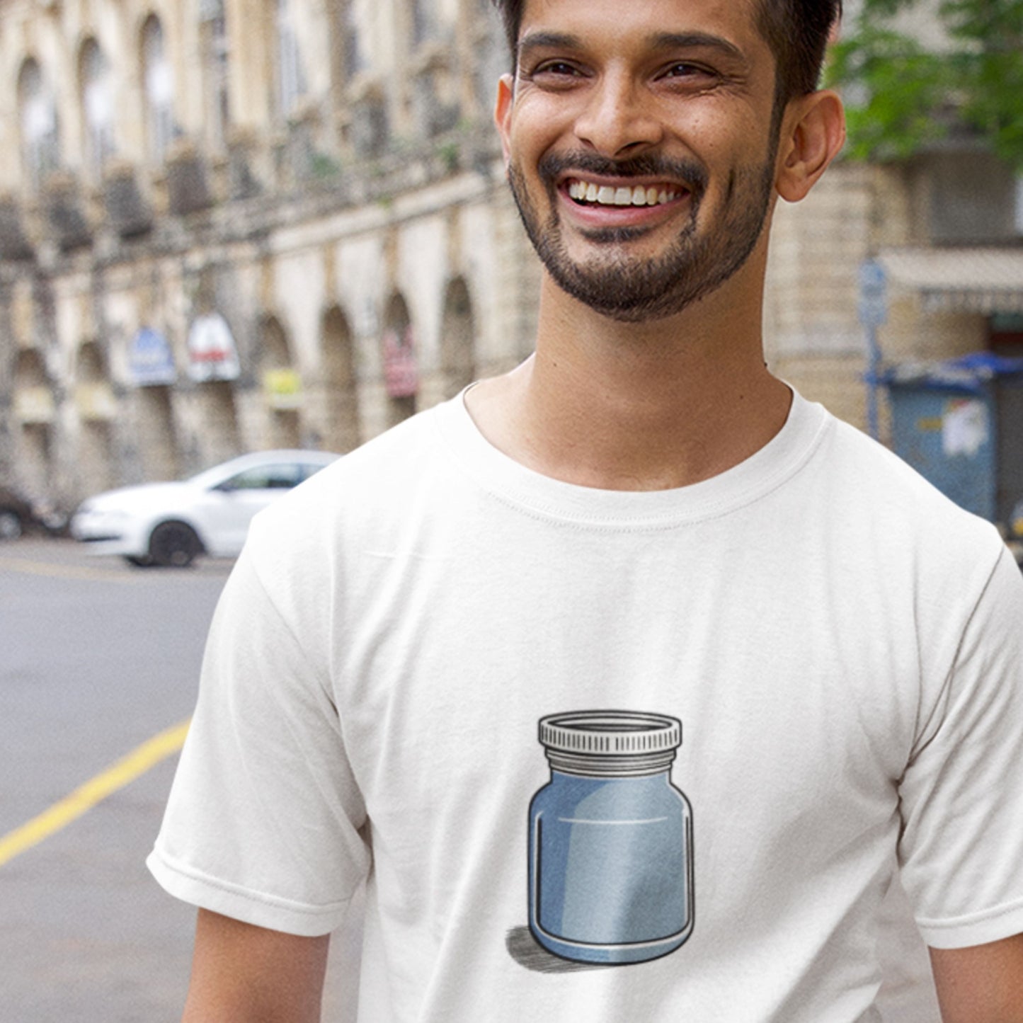 Man wearing a white t-shirt with a blue jar design on a city street.