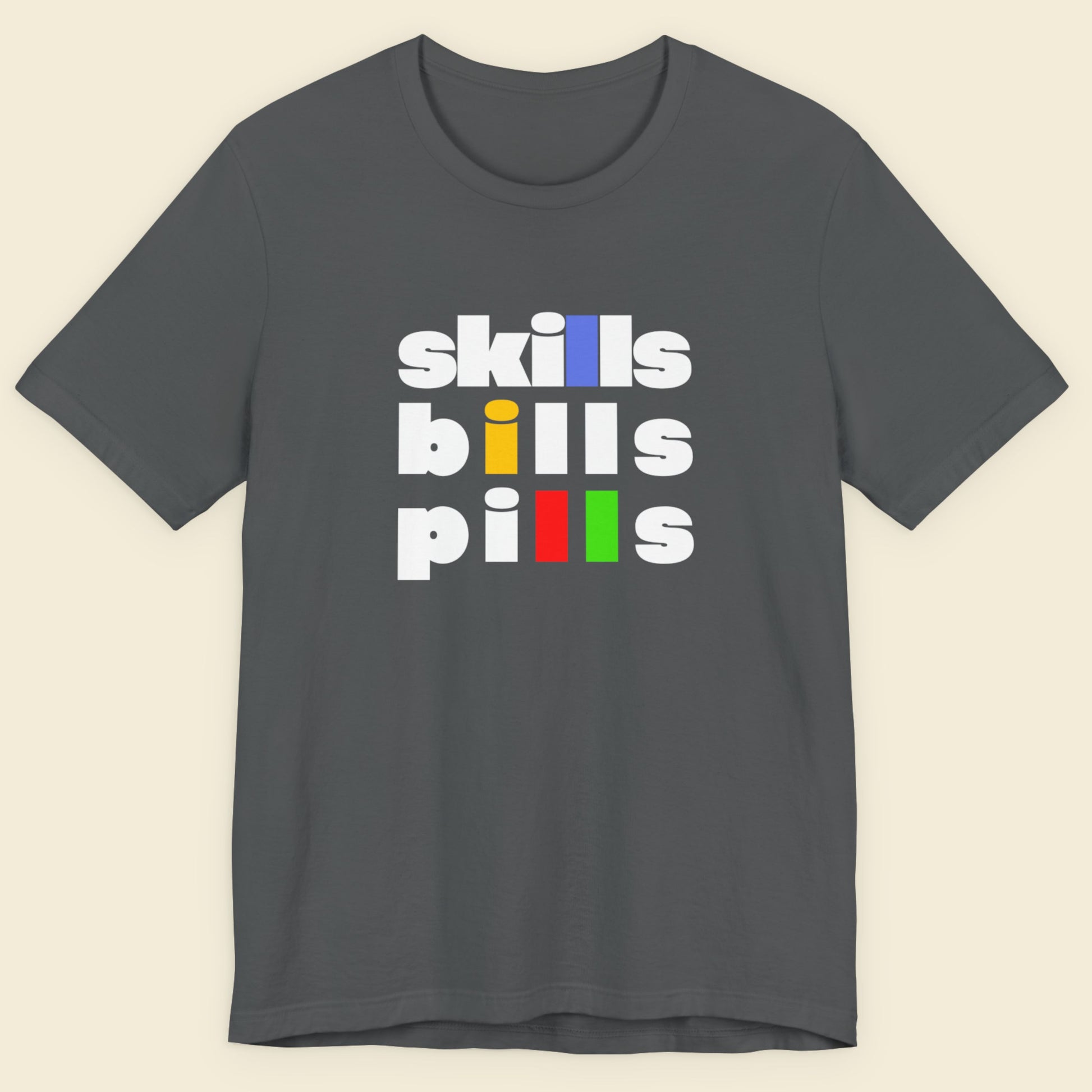 Grey t-shirt with 'skills bills pills' text in colorful letters on a beige background.