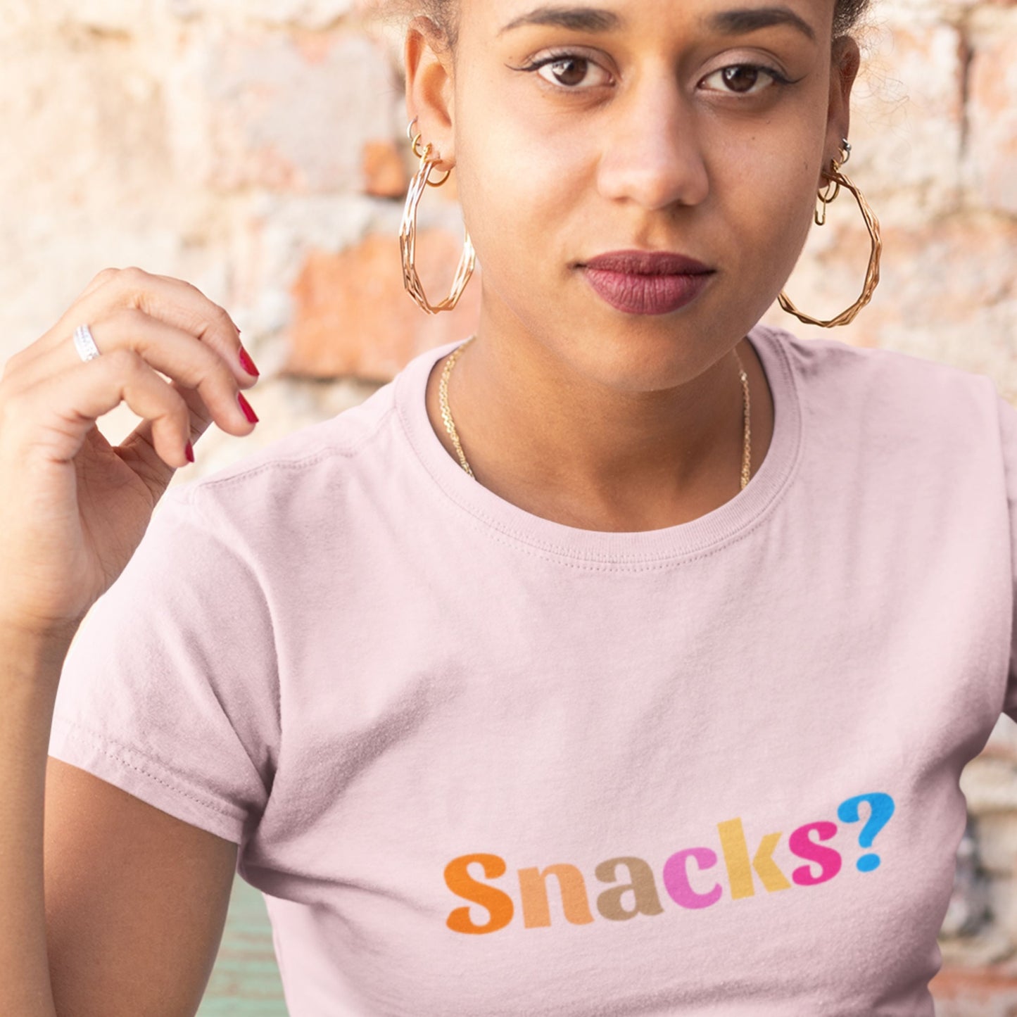 Woman wearing a light pink t-shirt with 'Snacks?' text in colorful letters.