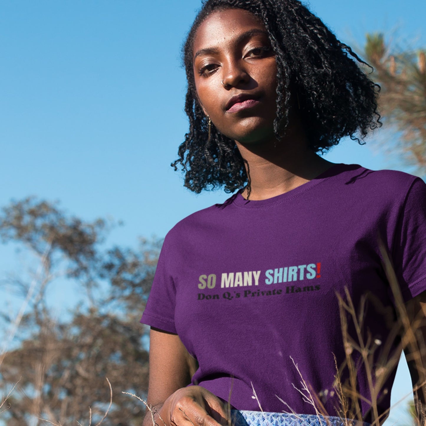Woman wearing a purple shirt with multicolored 'so many shirts!' text outside.