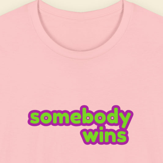 Pink t-shirt with multicolored 'somebody wins' text on a beige background.
