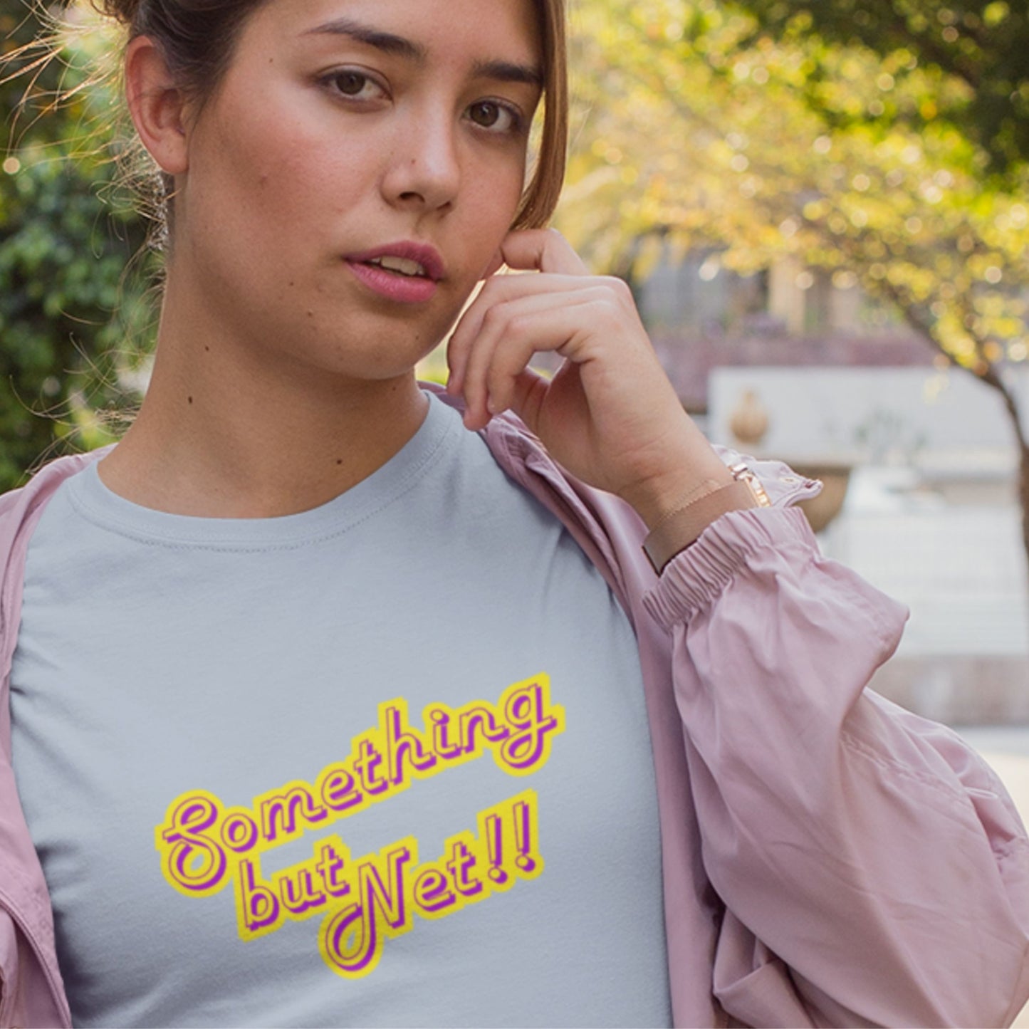 Woman wearing a light blue t-shirt with humorous colorful text outdoors.