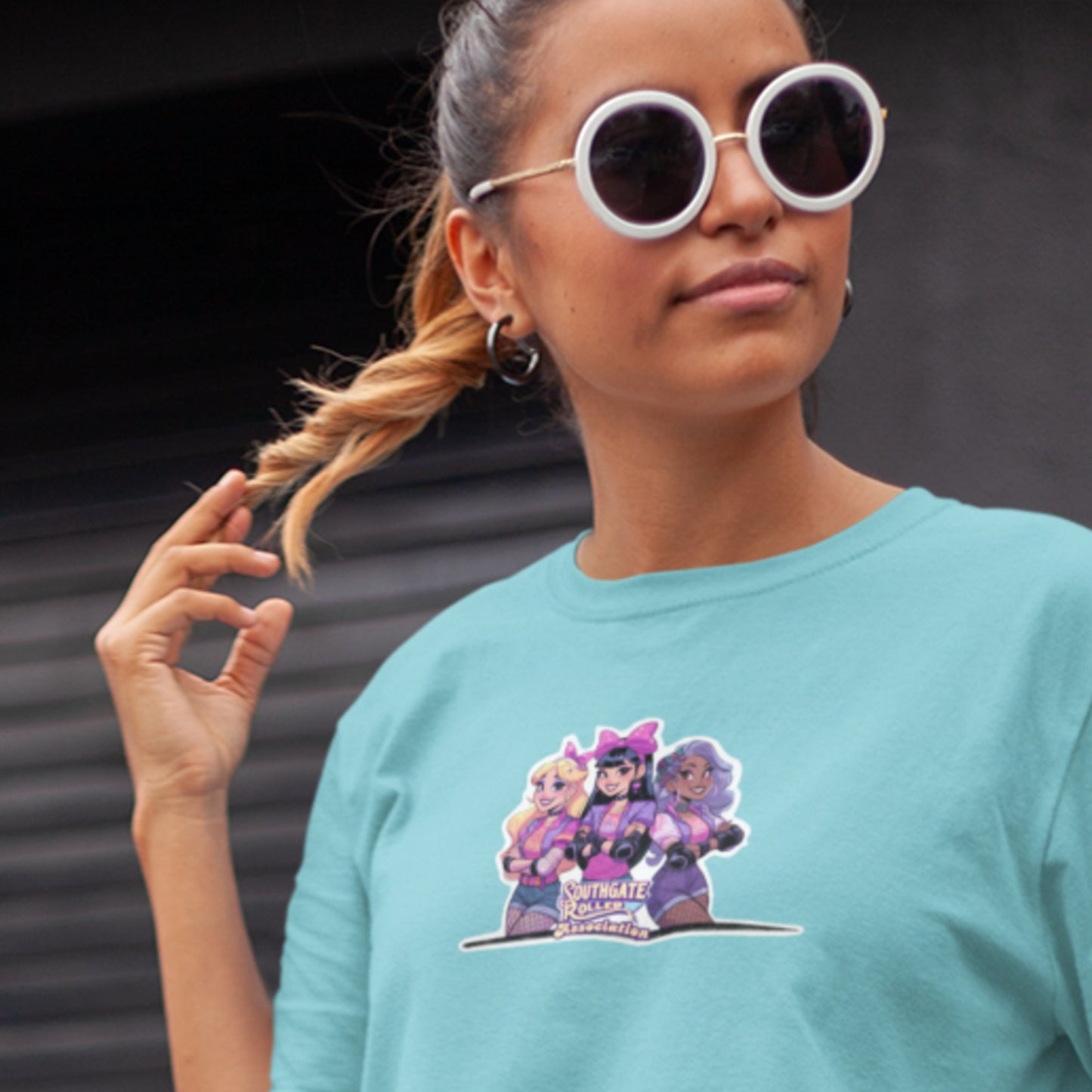 Model wearing a tuquoise shirt with a die cut sticker style graphic of famous power pop group, Southgate Roller Association