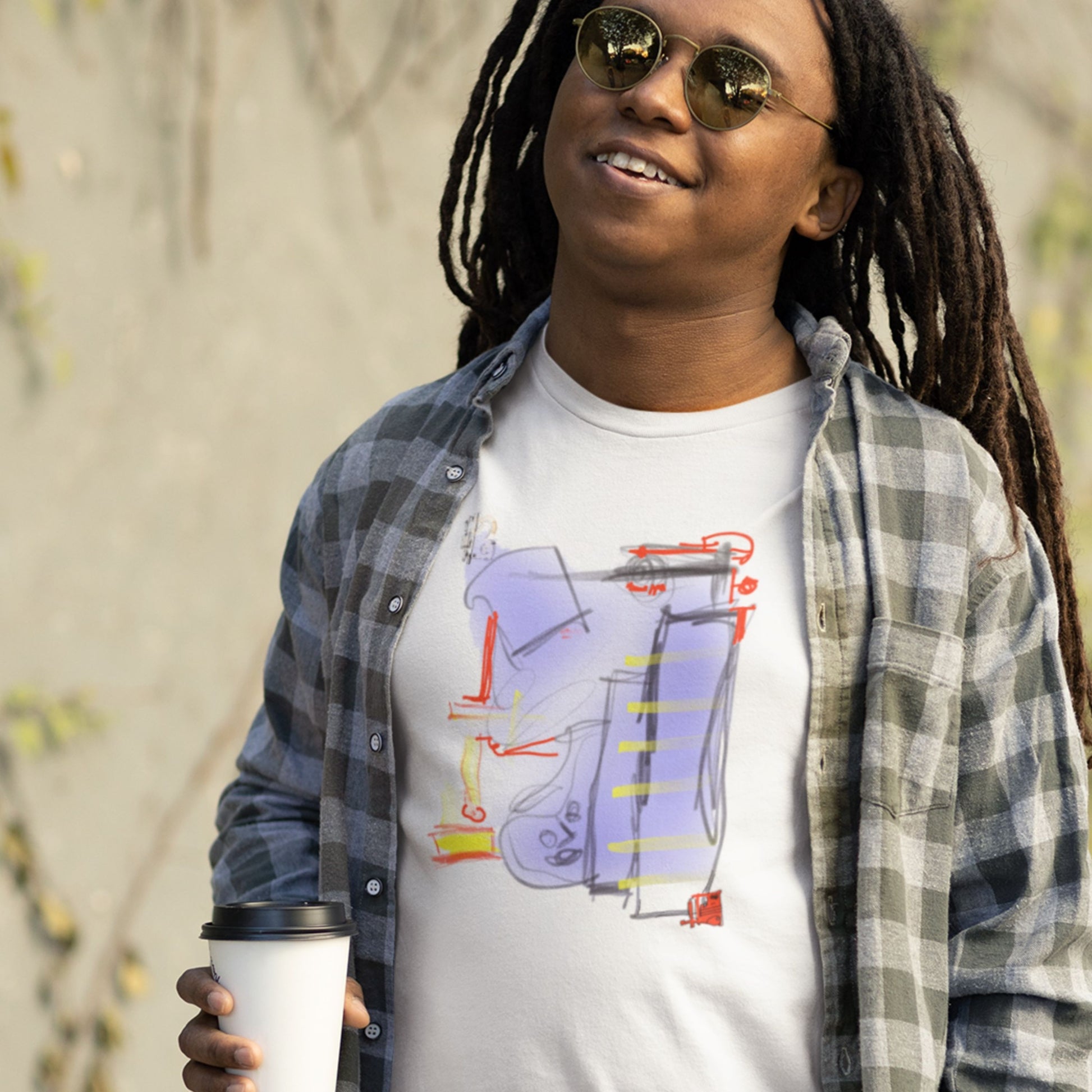 Man wearing a white t-shirt with a colorful abstract drawing outside with a coffee.