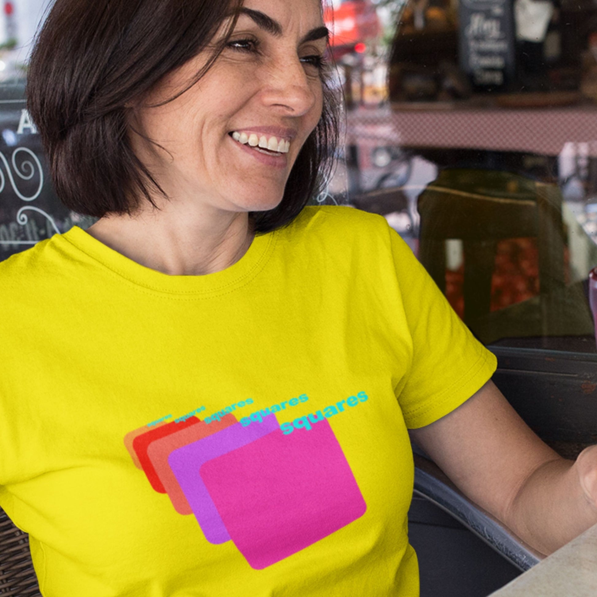 Woman wearing a bright yellow t-shirt with colorful graphic design in a casual setting.