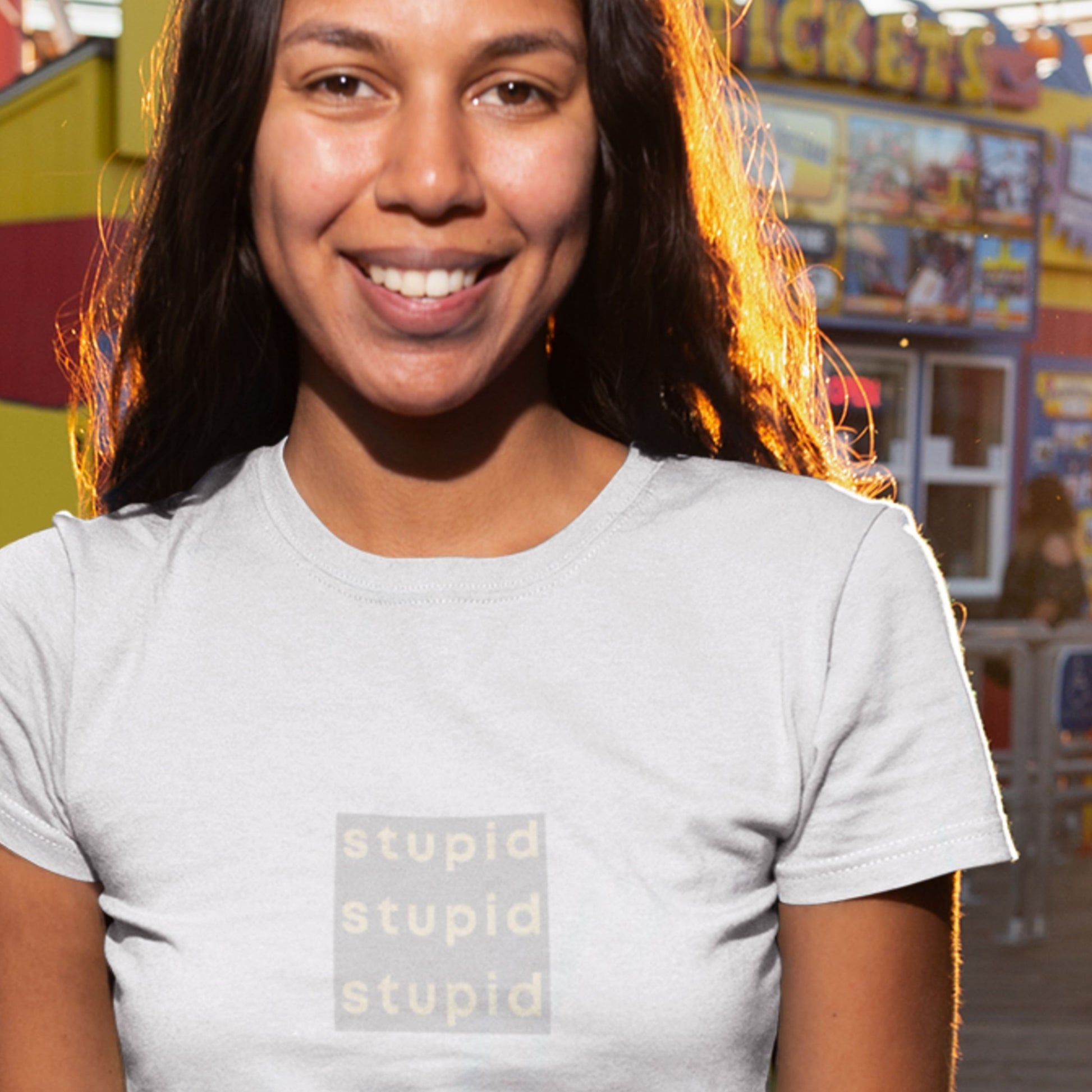Person wearing a gray t-shirt with 'stupid stupid stupid' text at an amusement park.