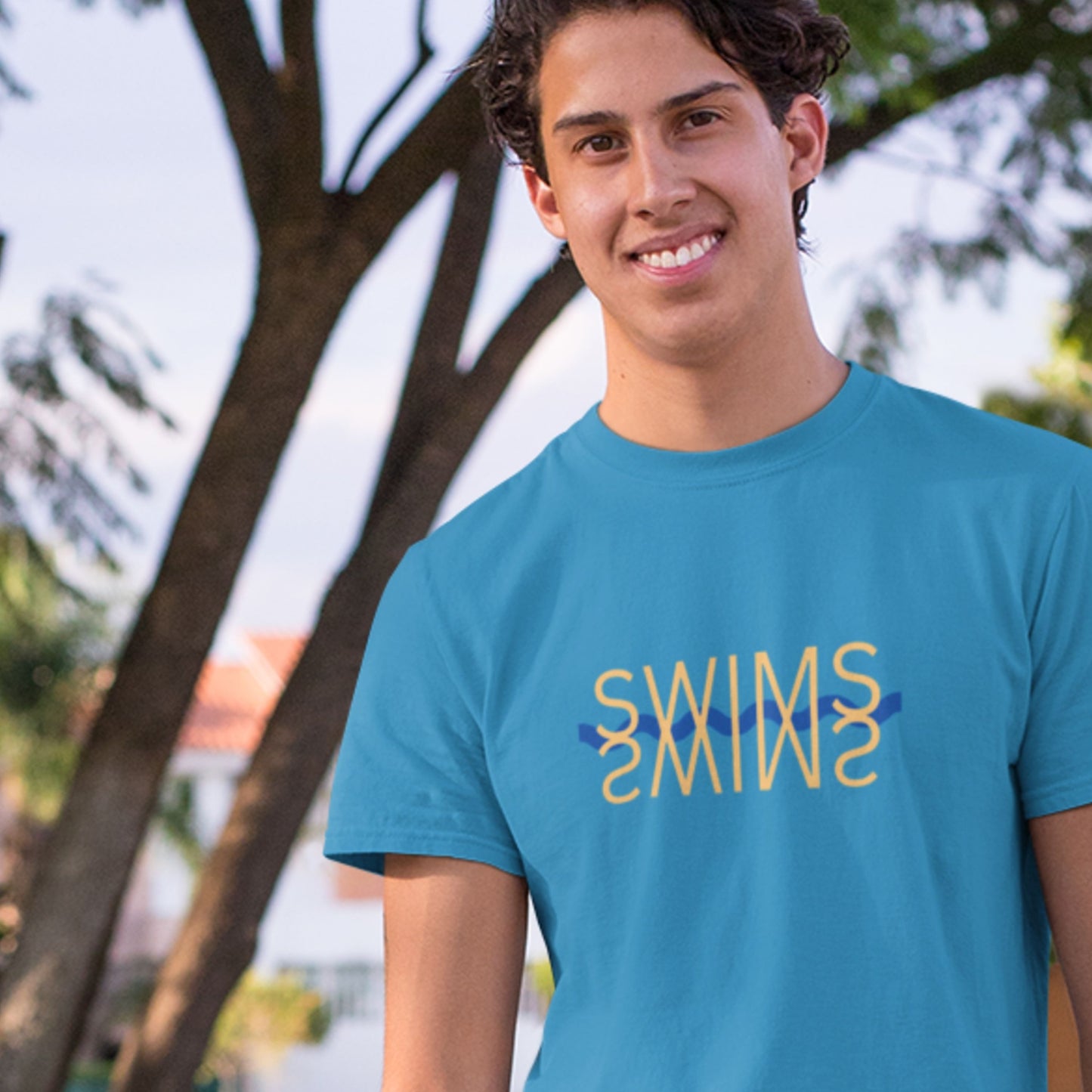 Man wearing a light blue t-shirt with humorous colorful text outdoors in front of trees.