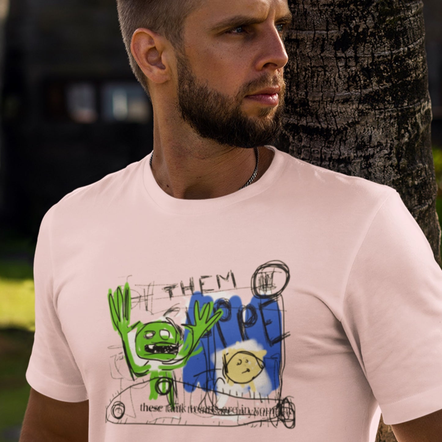 Man wearing a light pink t-shirt with a graphic design in an outdoor setting.