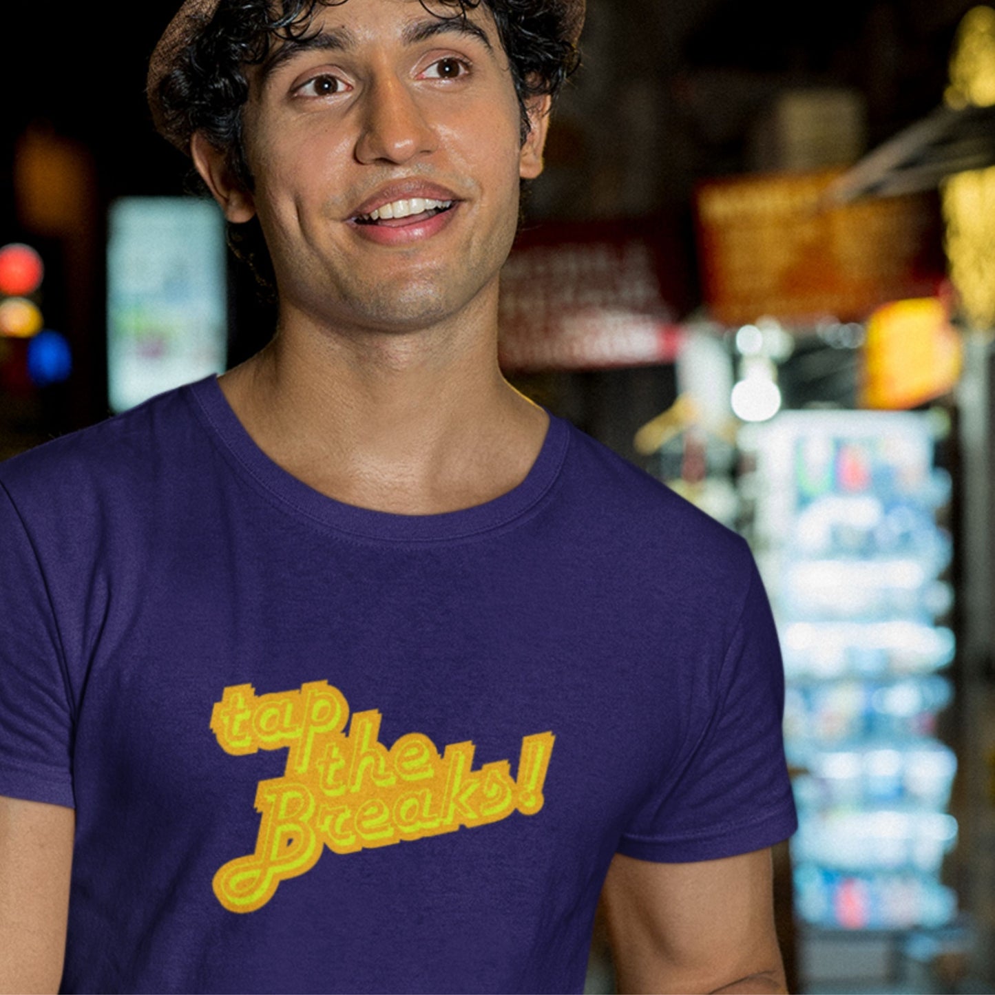 Smiling man wearing a navy t-shirt with humorous colorful text outside in a market.