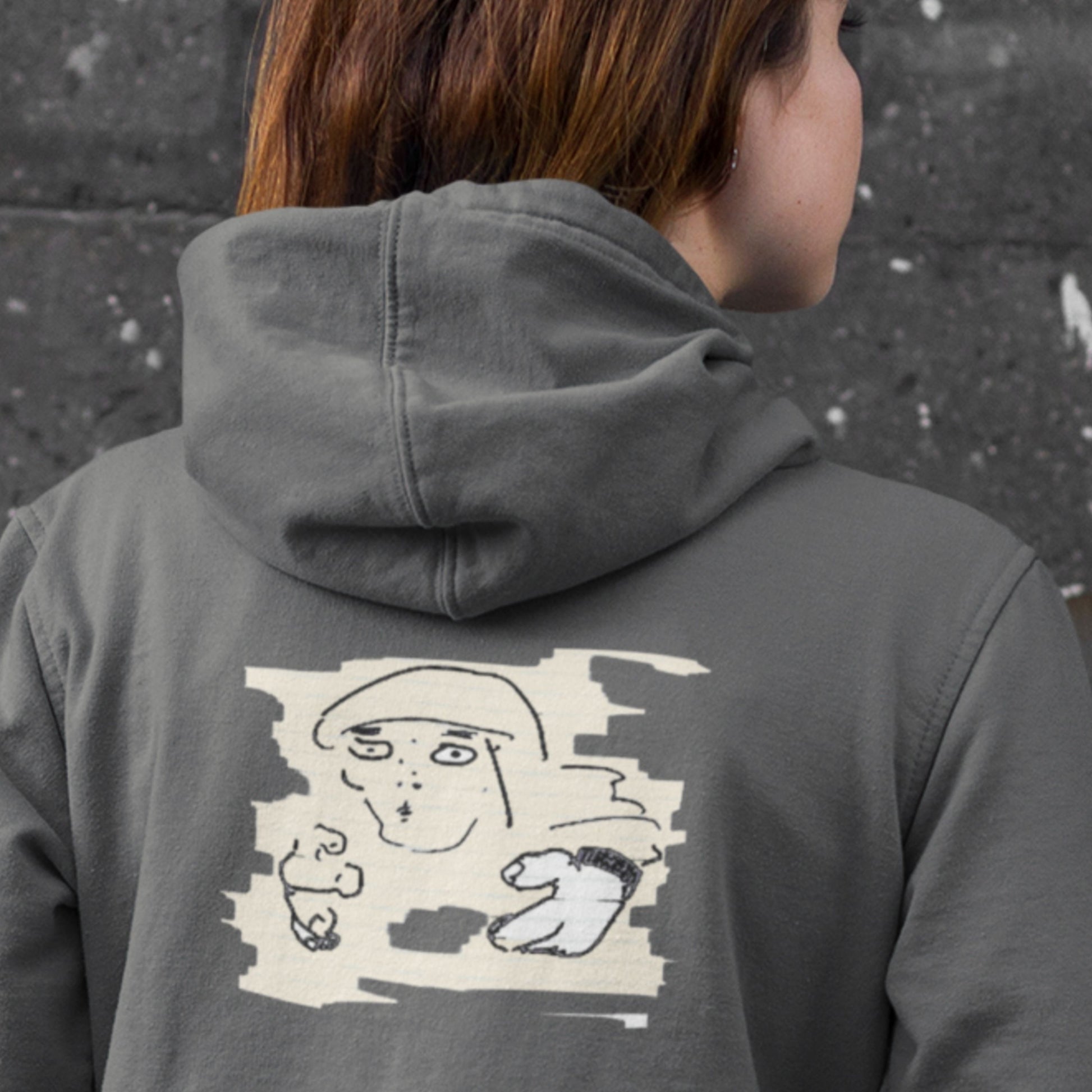 Person wearing a gray hoodie with a graphic design on the back against a dark wall.