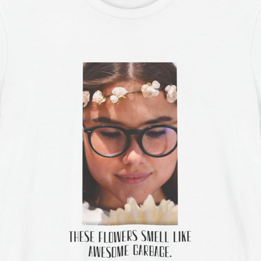 White t-shirt with a graphic of a woman wearing glasses and flowers, text 'These flowers smell like awesome garbage'.