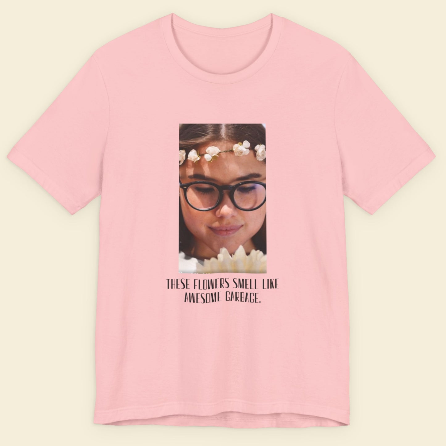 Pink t-shirt with a graphic of a person wearing glasses and flowers, and text on a beige background.