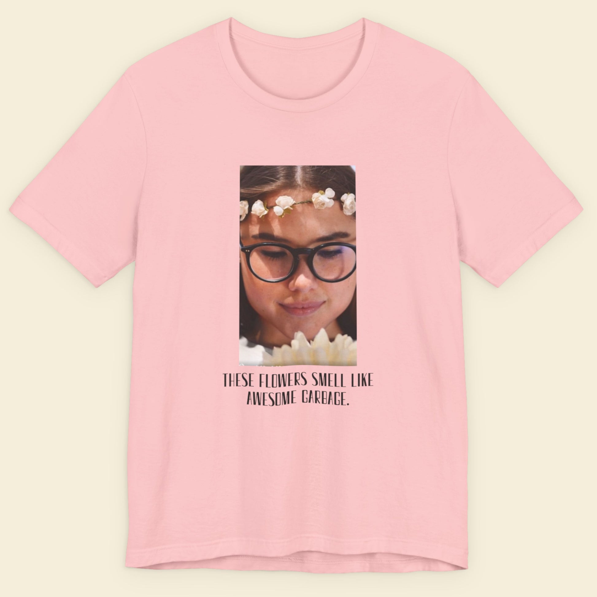 Pink t-shirt with a graphic of a person wearing glasses and flowers, and text on a beige background.