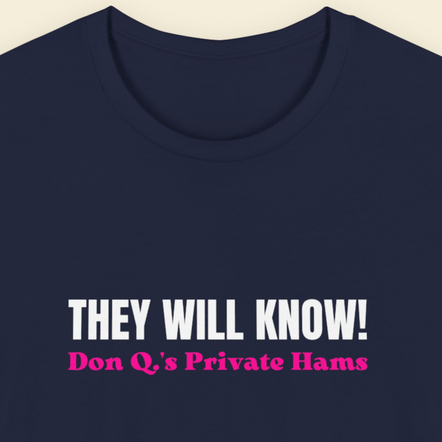 Navy blue t-shirt with white and pink text on a beige background.