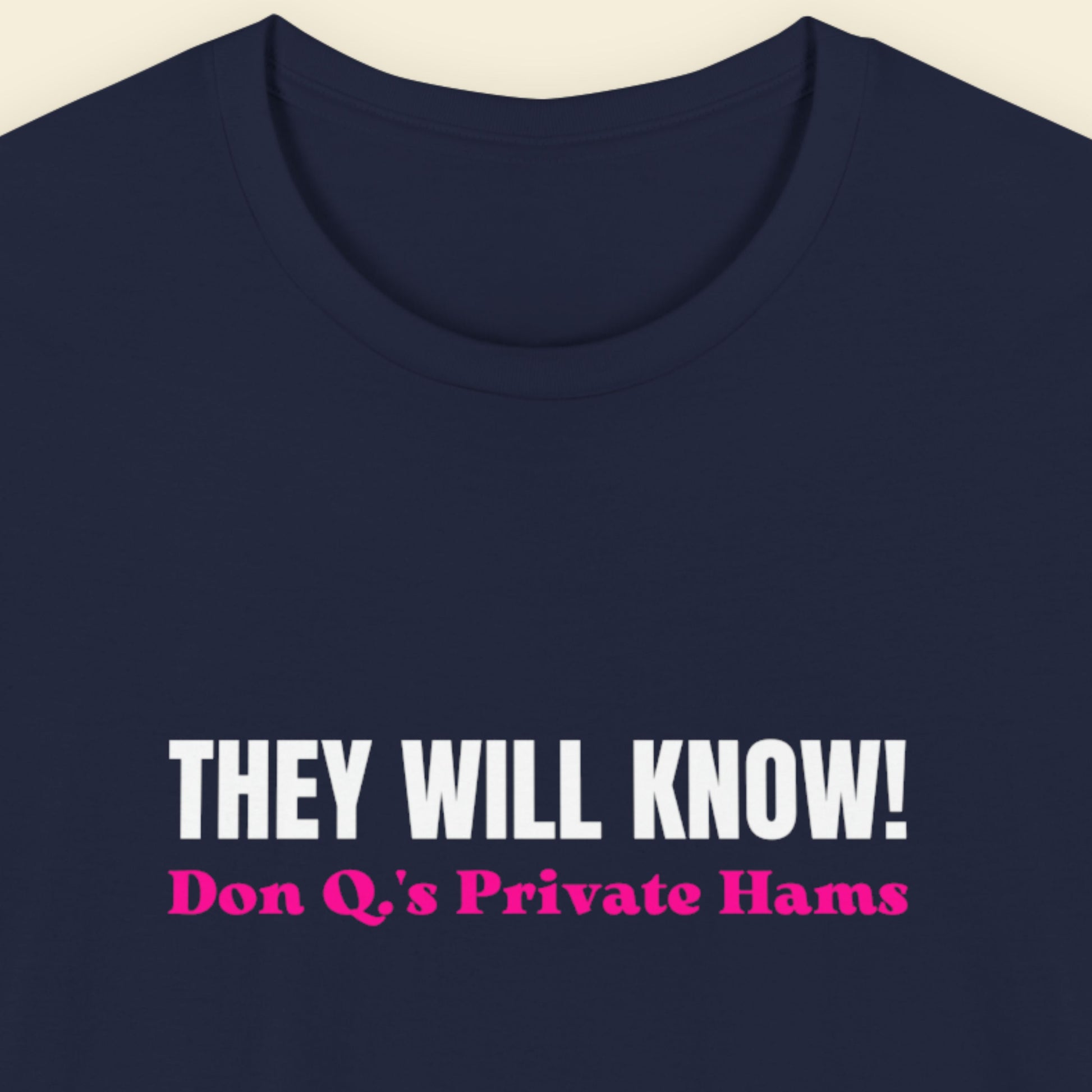 Navy blue t-shirt with white and pink text on a beige background.