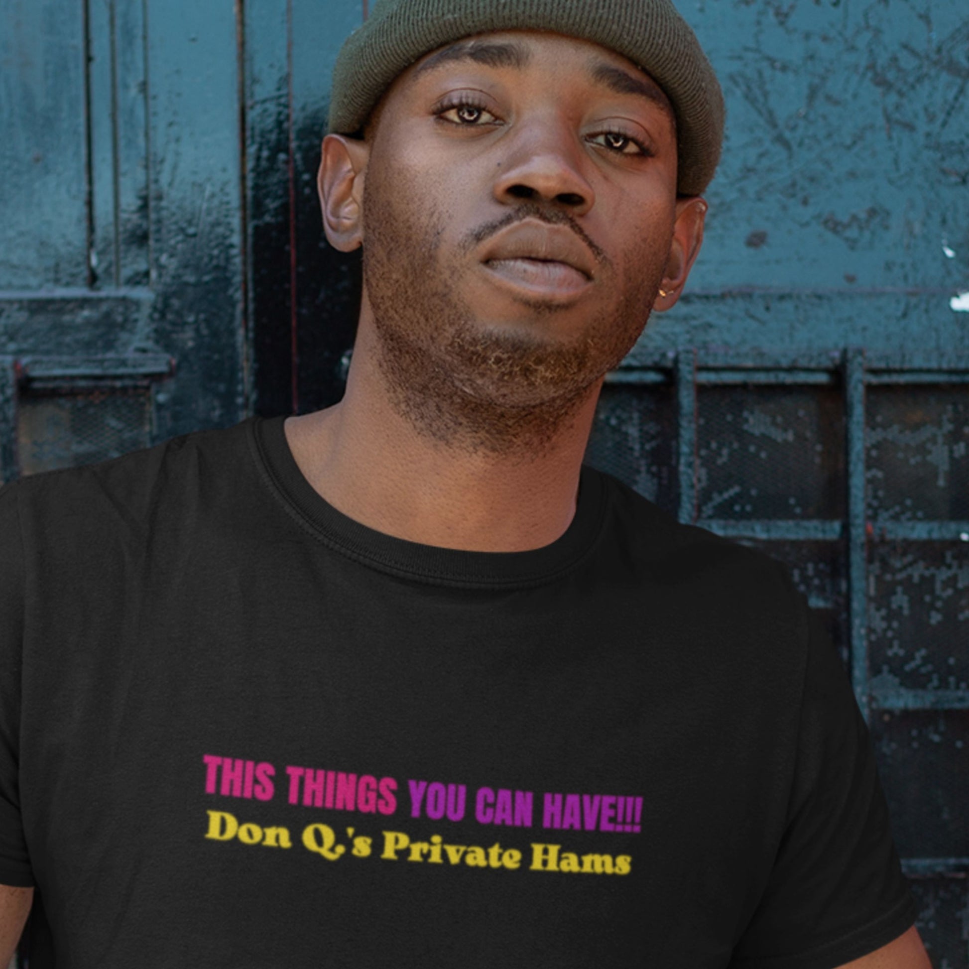 Man wearing a black t-shirt with colorful text in front of a textured wall.