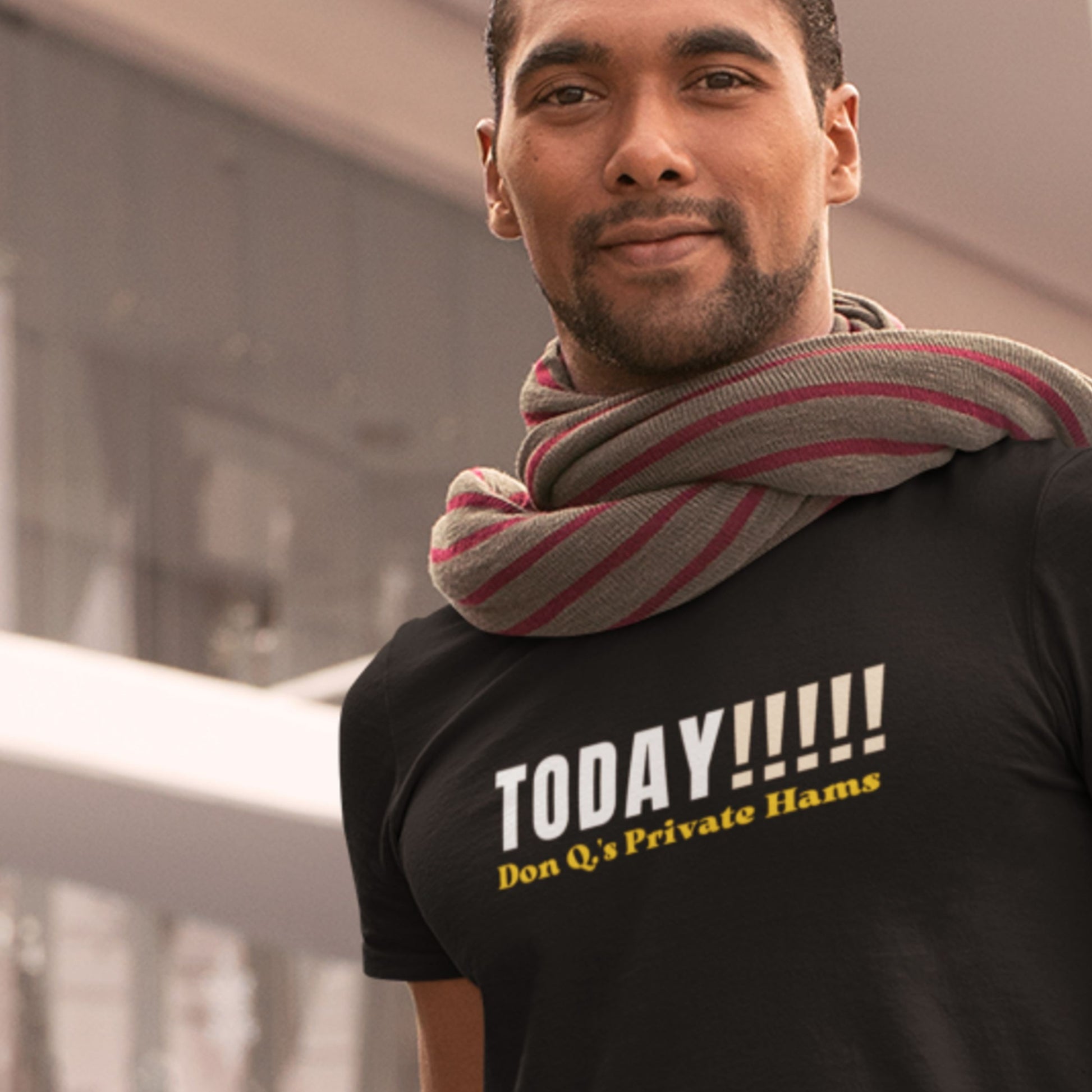 Man wearing a black t-shirt with text and a striped scarf, standing outdoors.