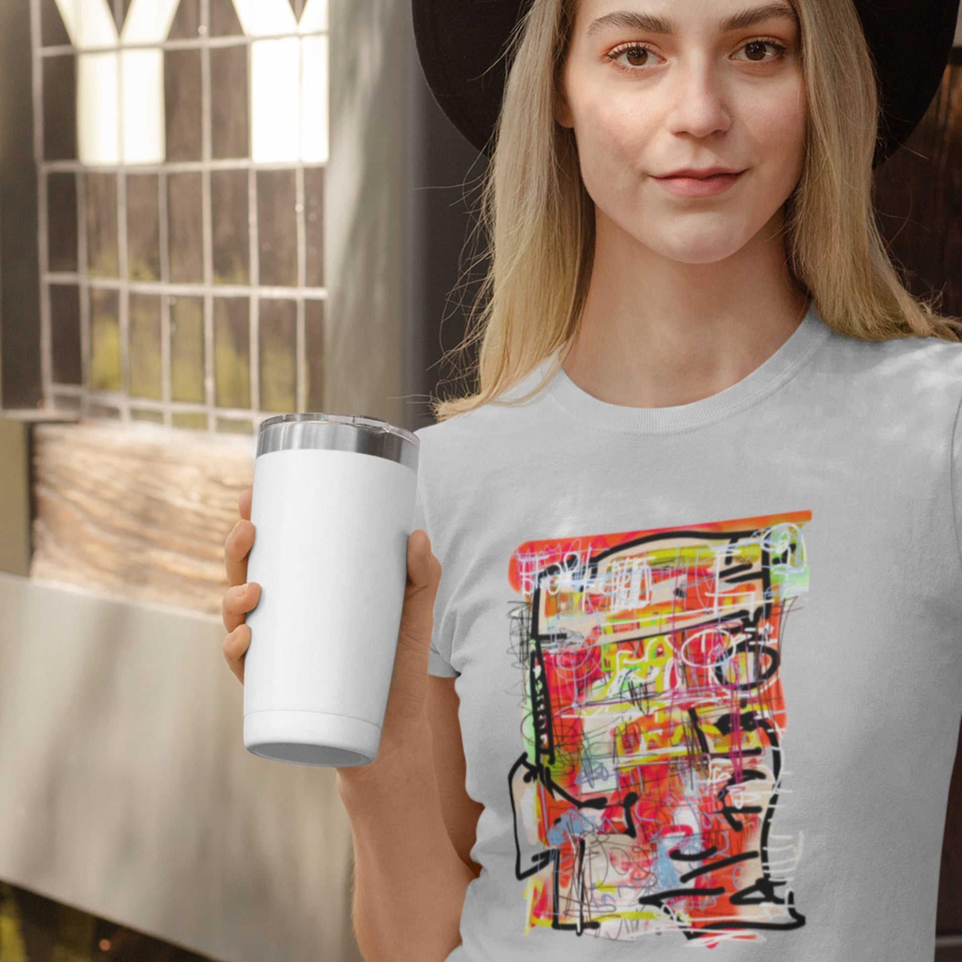 Person holding a white tumbler wearing a gray t-shirt with colorful graphic design.