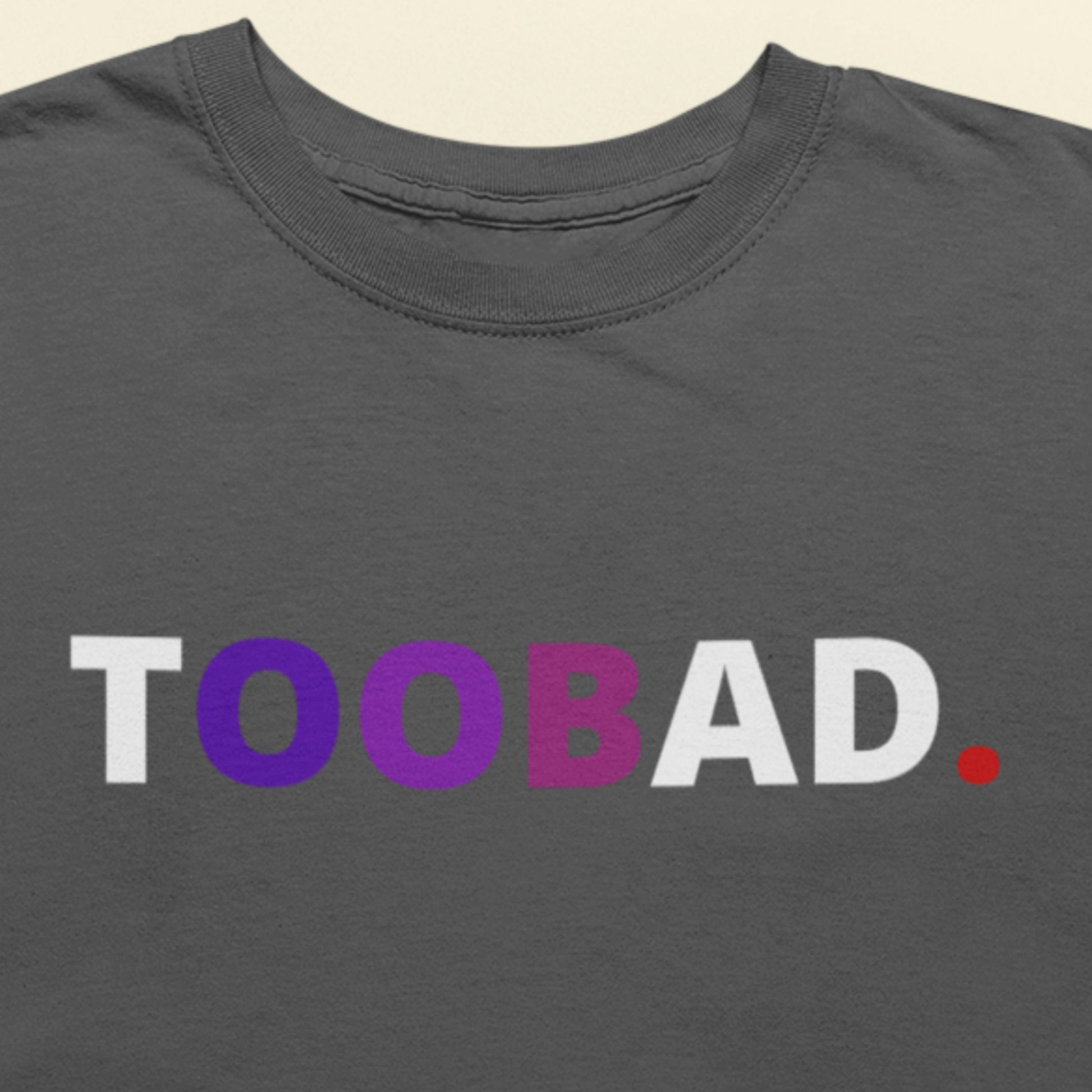 Gray t-shirt with 'TOOBAD.' text in white, purple, and red on a beige background