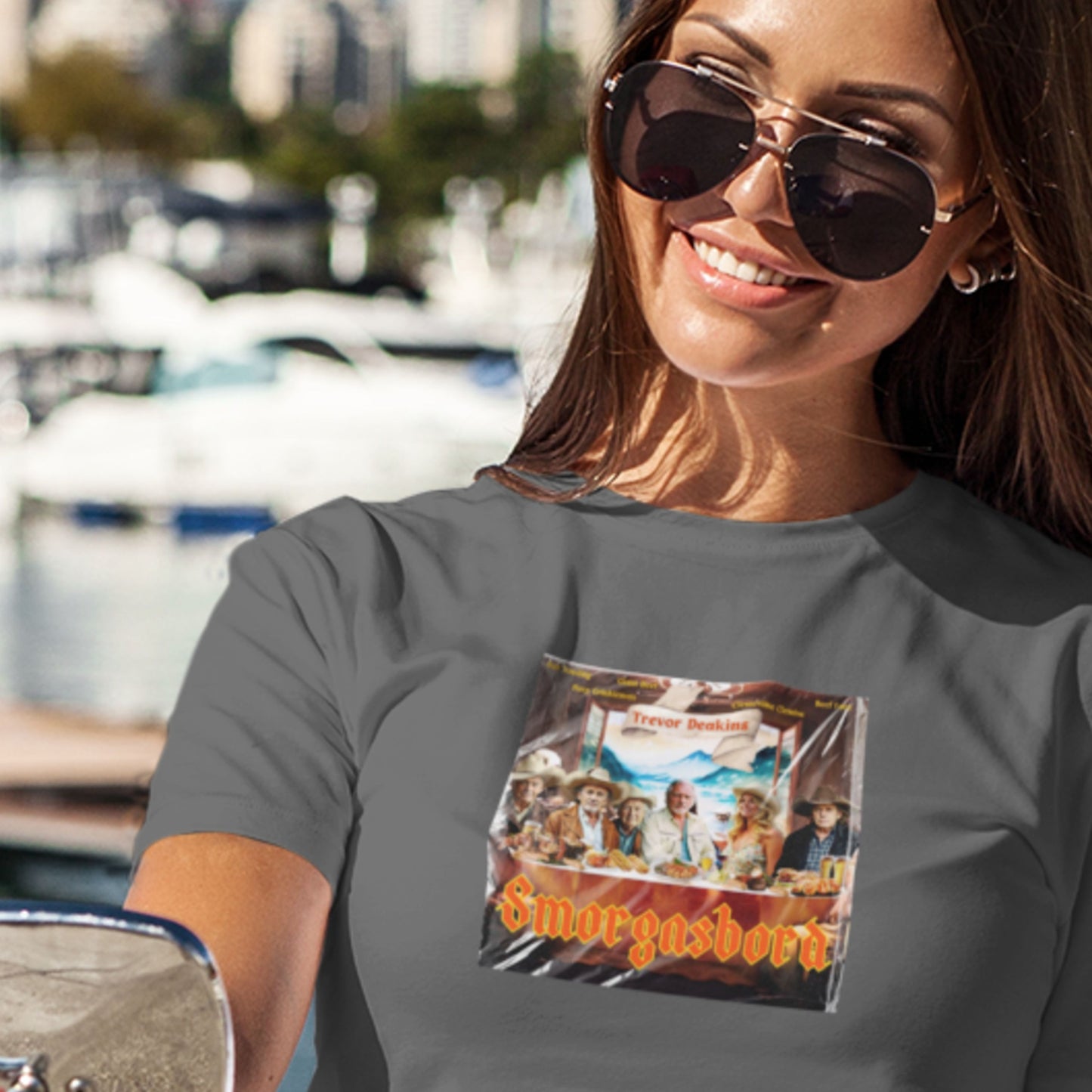 Woman wearing a t-shirt with a graphic design of people and text 'Smorgasbord' by a waterfront.