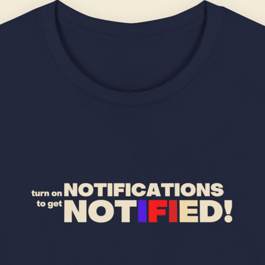 Navy blue t-shirt with colorful text 'turn on NOTIFICATIONS to get NOTIFIED!' on a beige background.