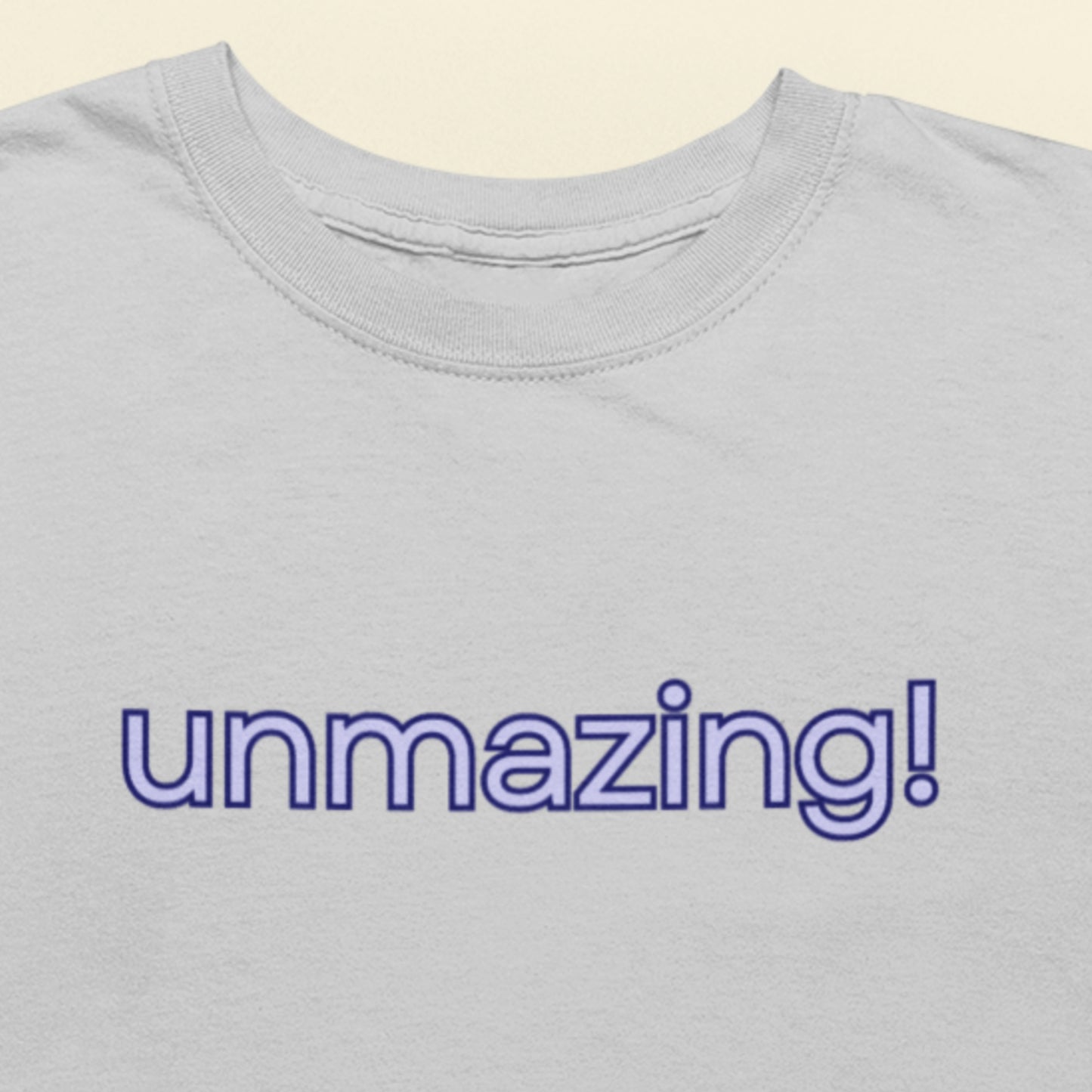 Gray t-shirt with 'unmazing!' text in purple on a beige background