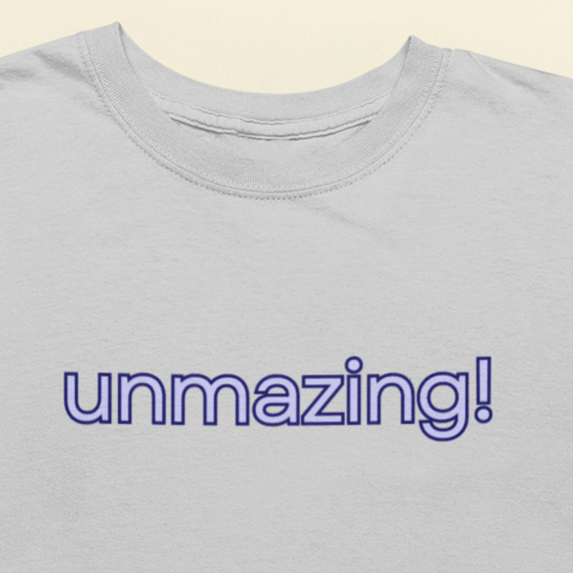 Gray t-shirt with 'unmazing!' text in purple on a beige background