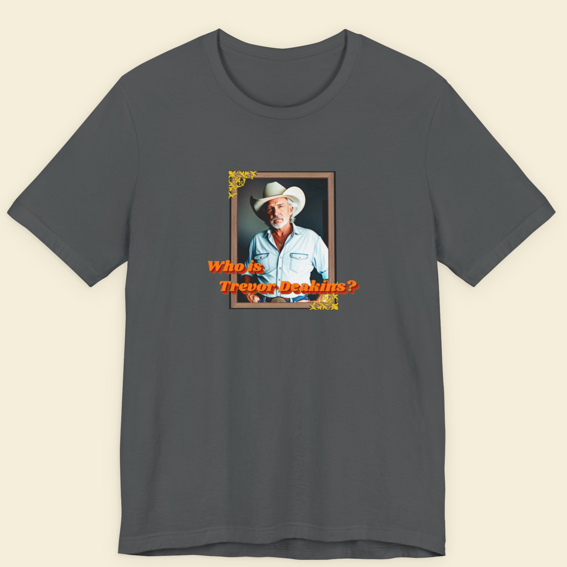 Gray t-shirt with a graphic of a man in a cowboy hat and text 'Who is Trevor Deakins?' on a beige background