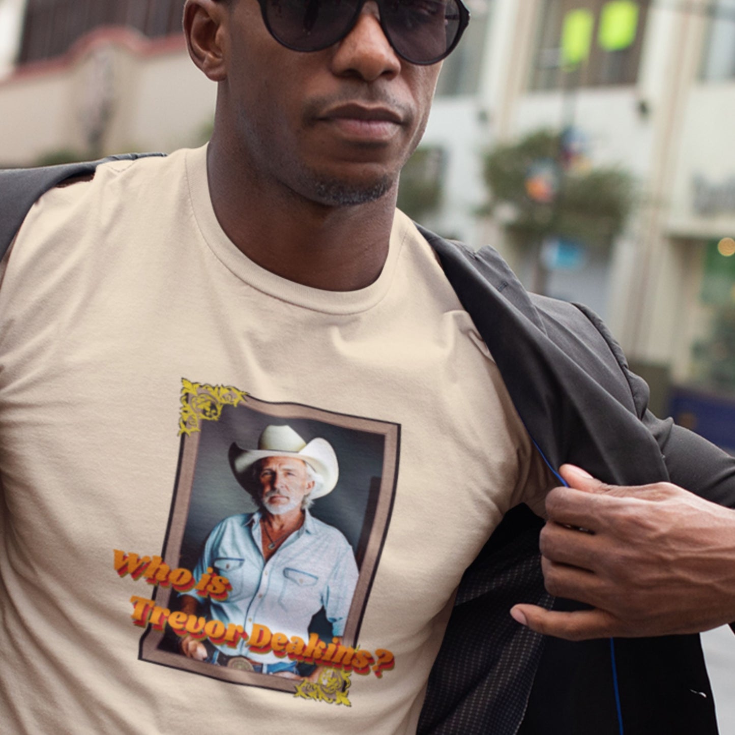 Man wearing a beige t-shirt with a graphic of a man in a cowboy hat and text, standing outdoors.