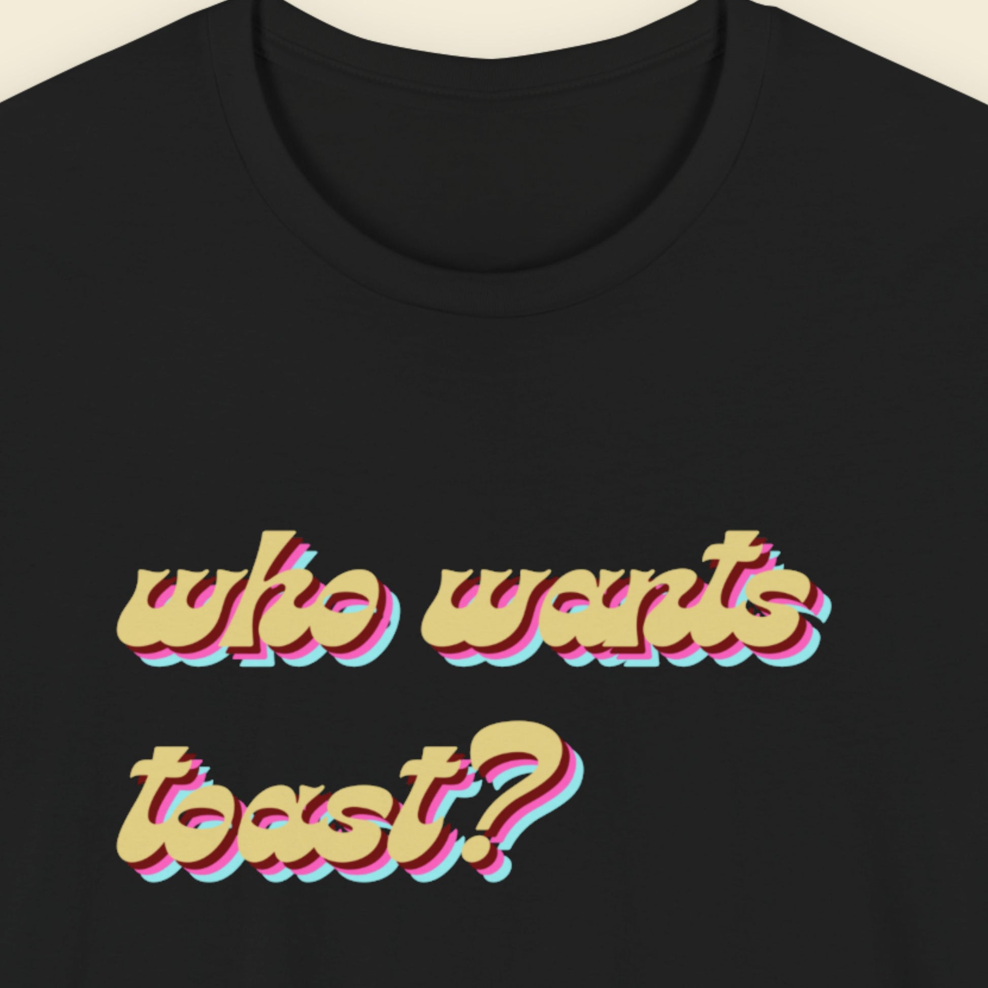Black t-shirt with colorful text 'who wants toast?' on a beige background.