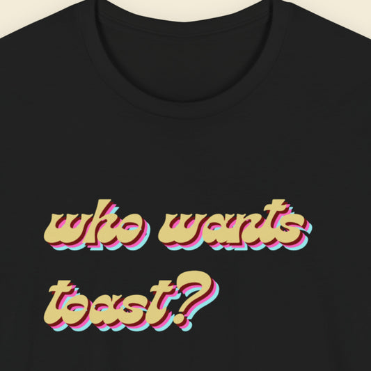 Black t-shirt with colorful text 'who wants toast?' on a beige background.