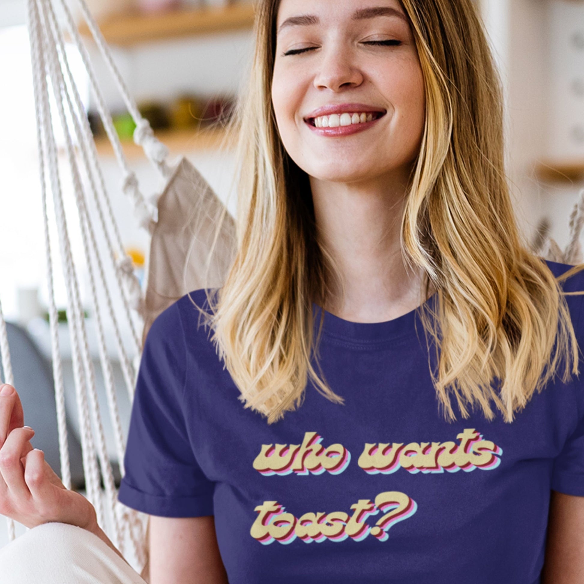 Woman wearing a purple t-shirt with 'who wants toast?' text, smiling indoors.