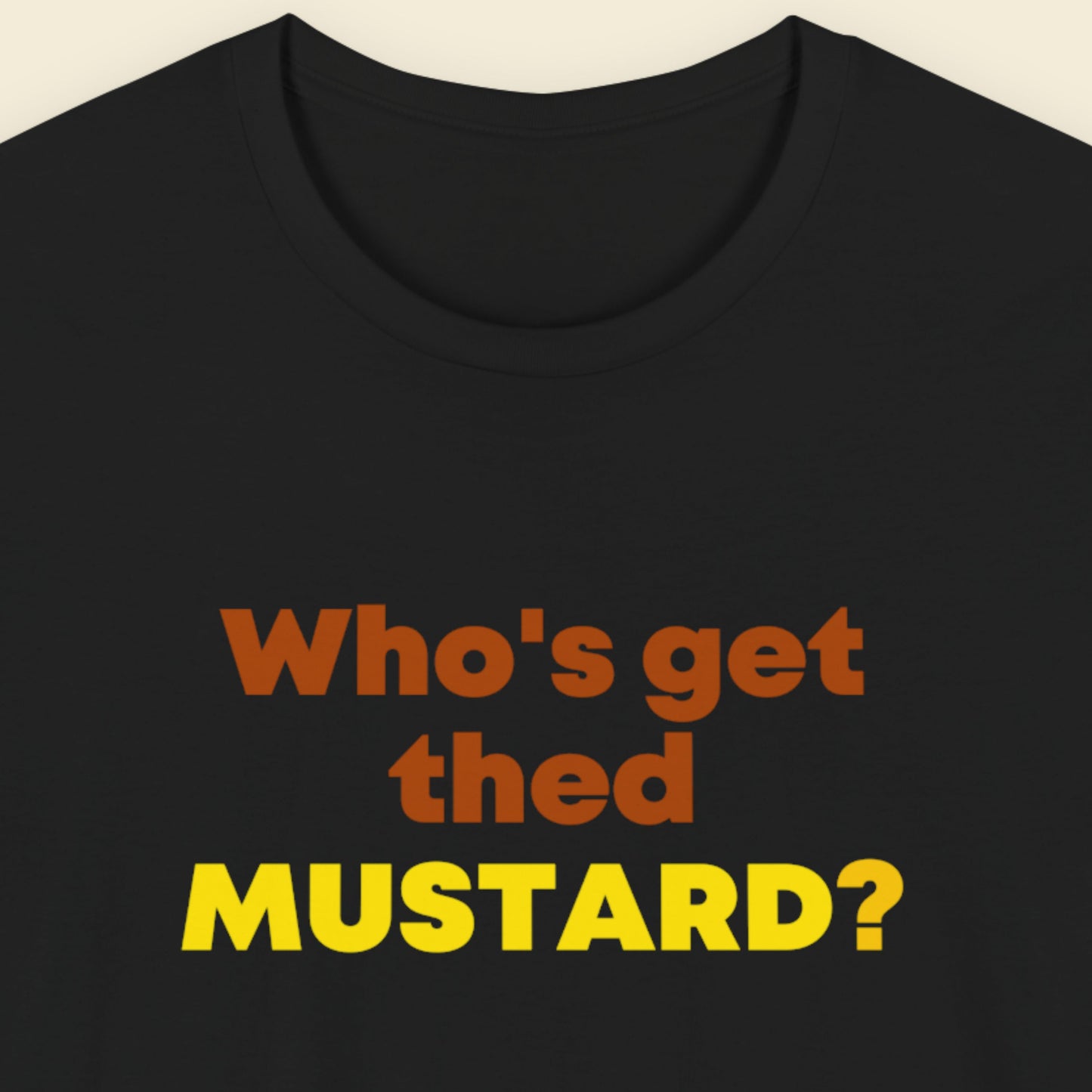 Black t-shirt with colorful text 'Who's get thed MUSTARD?' on a beige background.