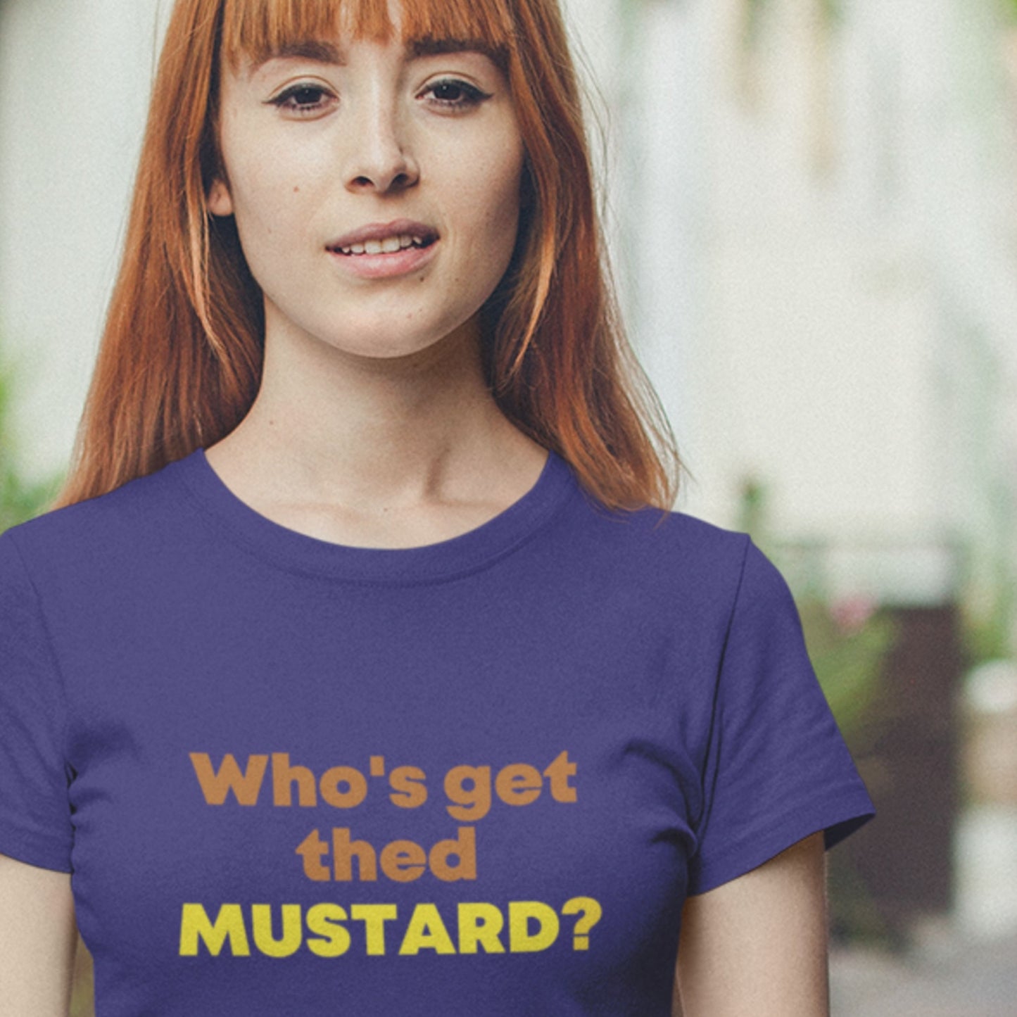 Person wearing a purple t-shirt with text 'Who's get thed MUSTARD?' in an outdoor setting.